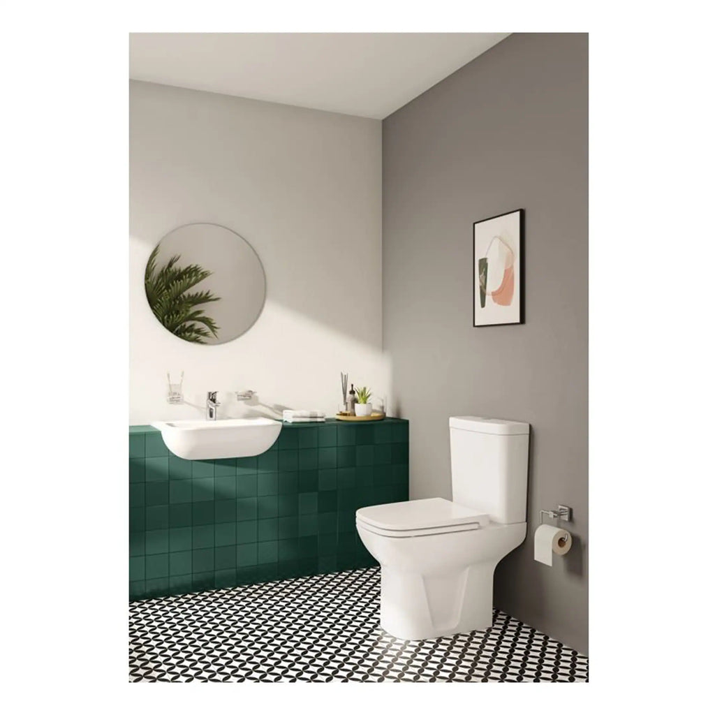 Sleek modern bathroom with white toilet and green tiled vanity unit, minimalist sink with chrome fixtures, black and white patterned floor, wall art, and a round mirror reflecting green foliage, creating a stylish and functional space.