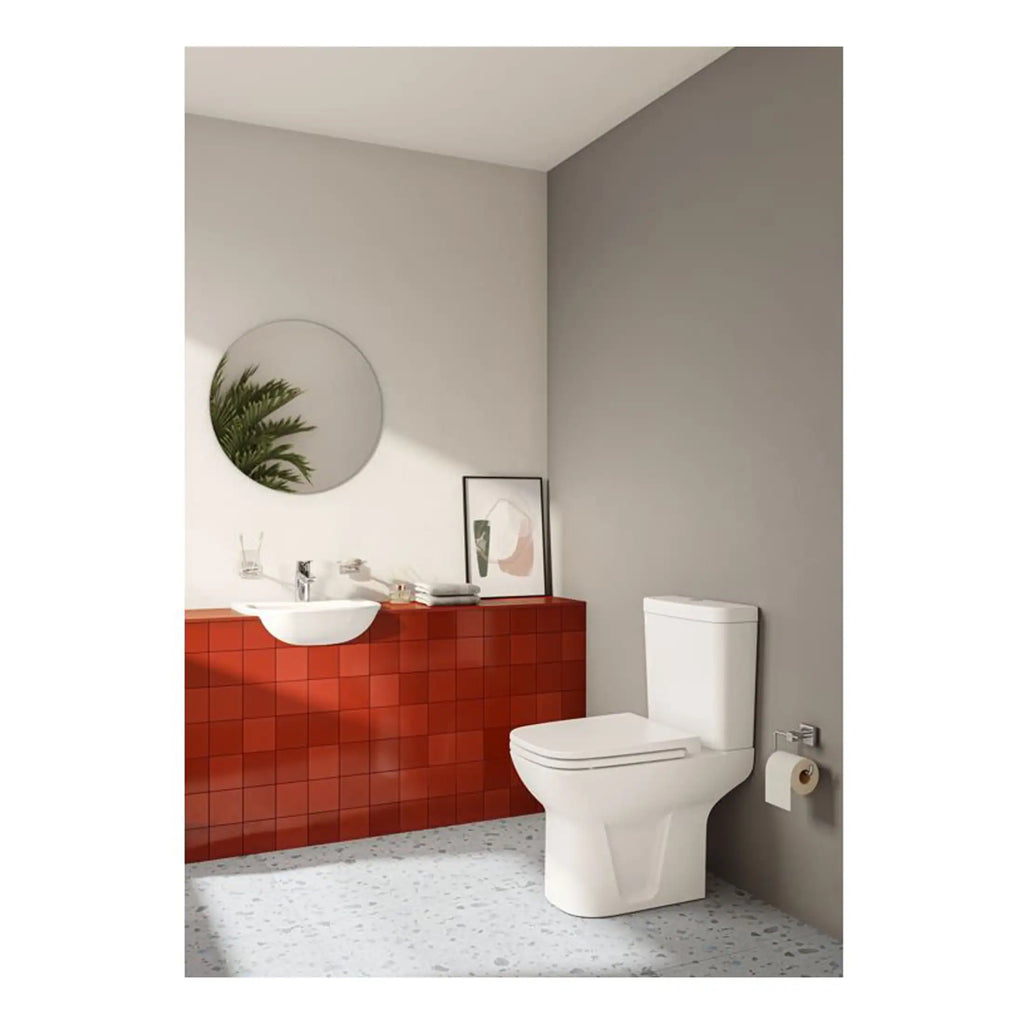 Sleek modern bathroom featuring a white toilet, a minimalist wall-mounted sink, stylish red tile paneling, and contemporary decor with a round mirror and framed artwork.
