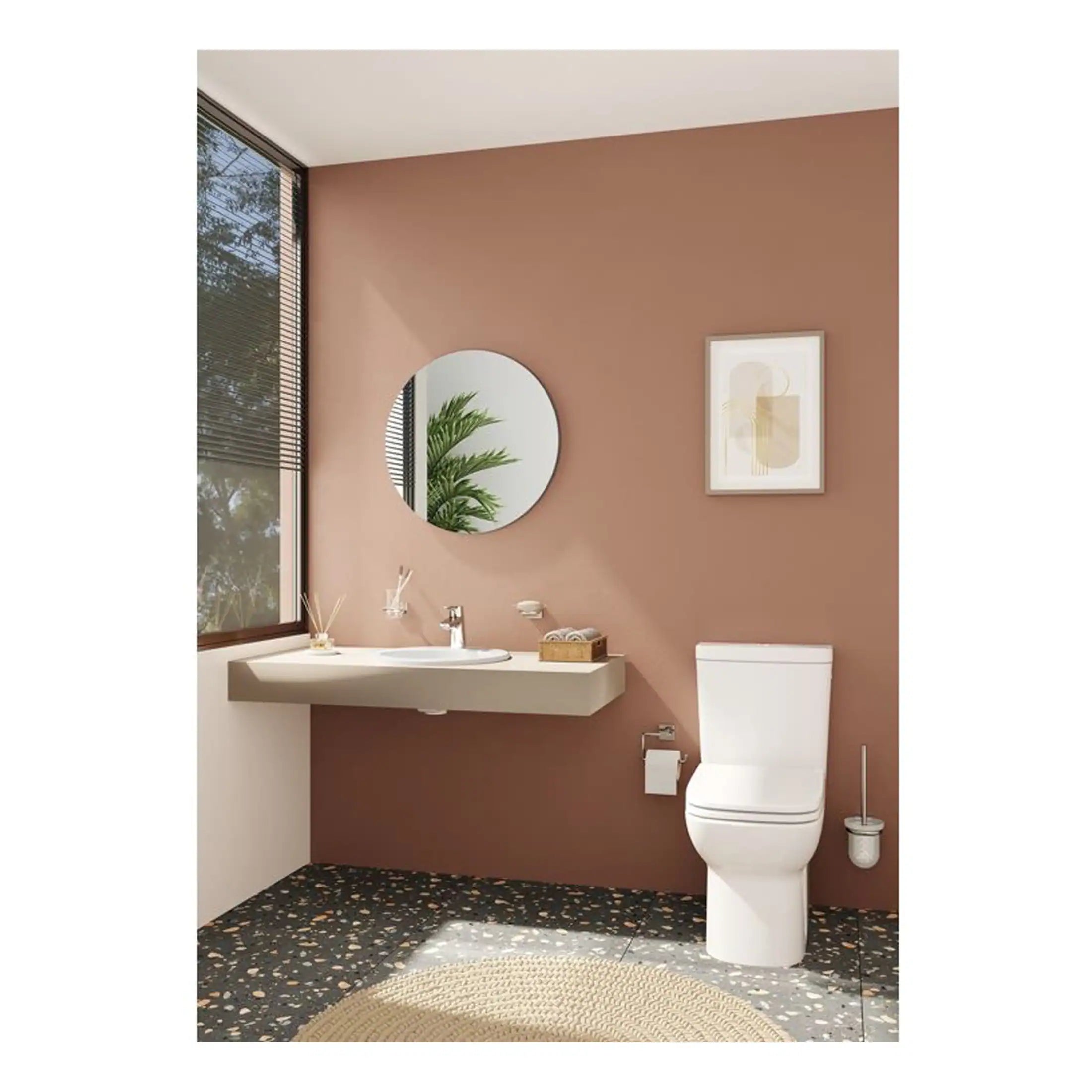 Modern bathroom with beige wall, white toilet and minimalist sink, decorated with framed abstract art and a round mirror, natural light from large window, stylish and functional design for contemporary bathroom spaces.
