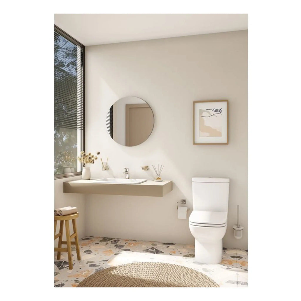 Bright modern bathroom with minimalist design, white toilet, floating vanity with round mirror, decorative artwork, natural light from large window, and terrazzo flooring for a stylish look.