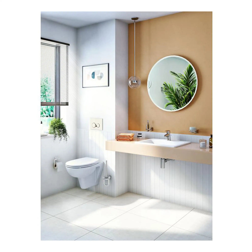 Modern minimalist bathroom featuring a sleek wall-mounted toilet, a stylish beige vanity with a white sink, a round mirror, and natural light from a window, decorated with potted plants for a fresh look.