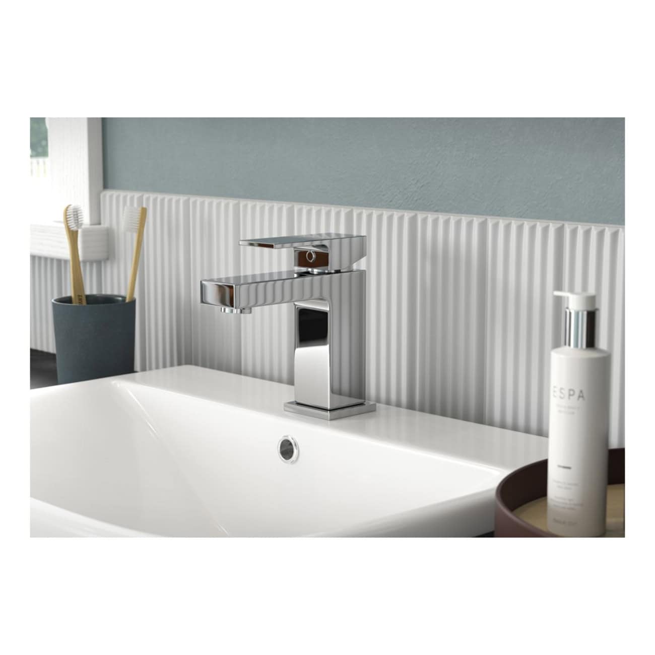 Sleek modern chrome bathroom faucet with minimalist design, installed above a white ceramic sink, accompanied by toothbrushes and bathroom essentials in a contemporary bathroom setting.