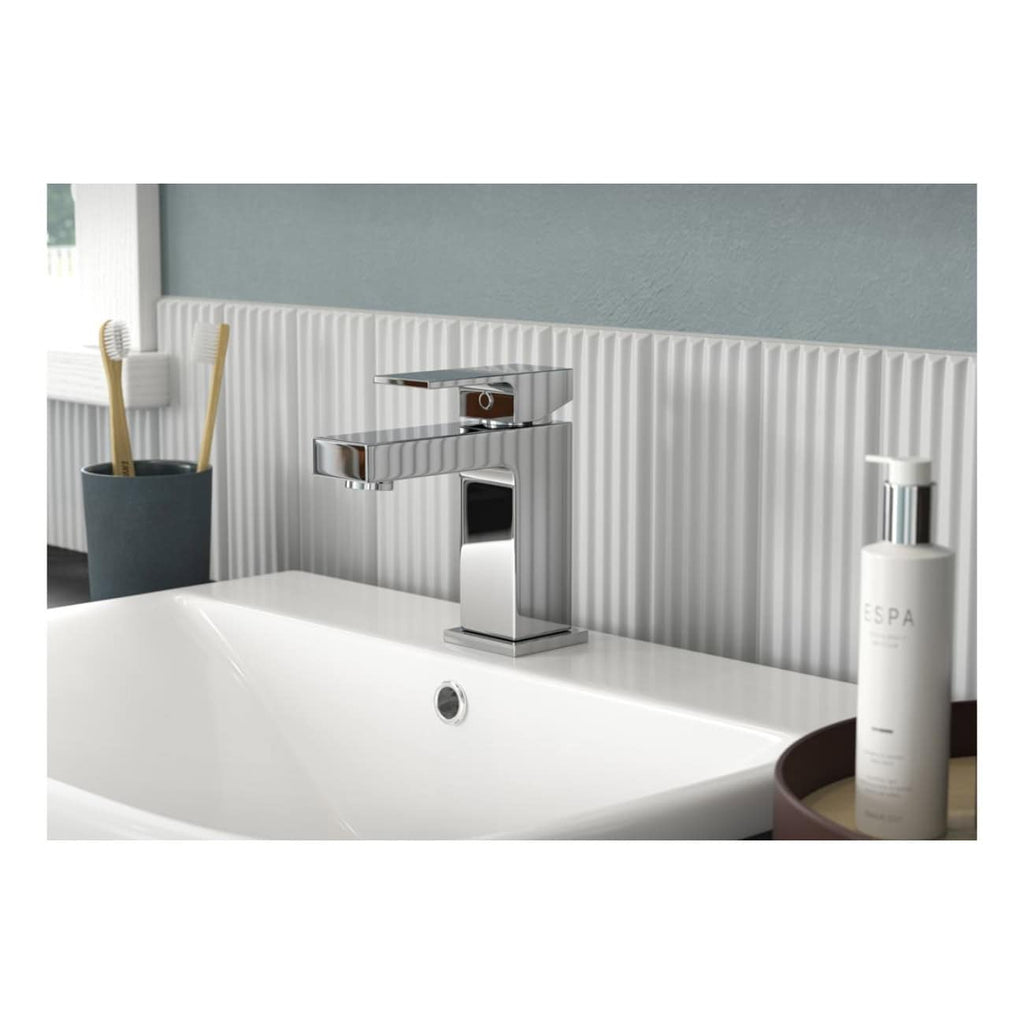 Sleek modern chrome bathroom faucet with minimalist design, installed above a white ceramic sink, accompanied by toothbrushes and bathroom essentials in a contemporary bathroom setting.
