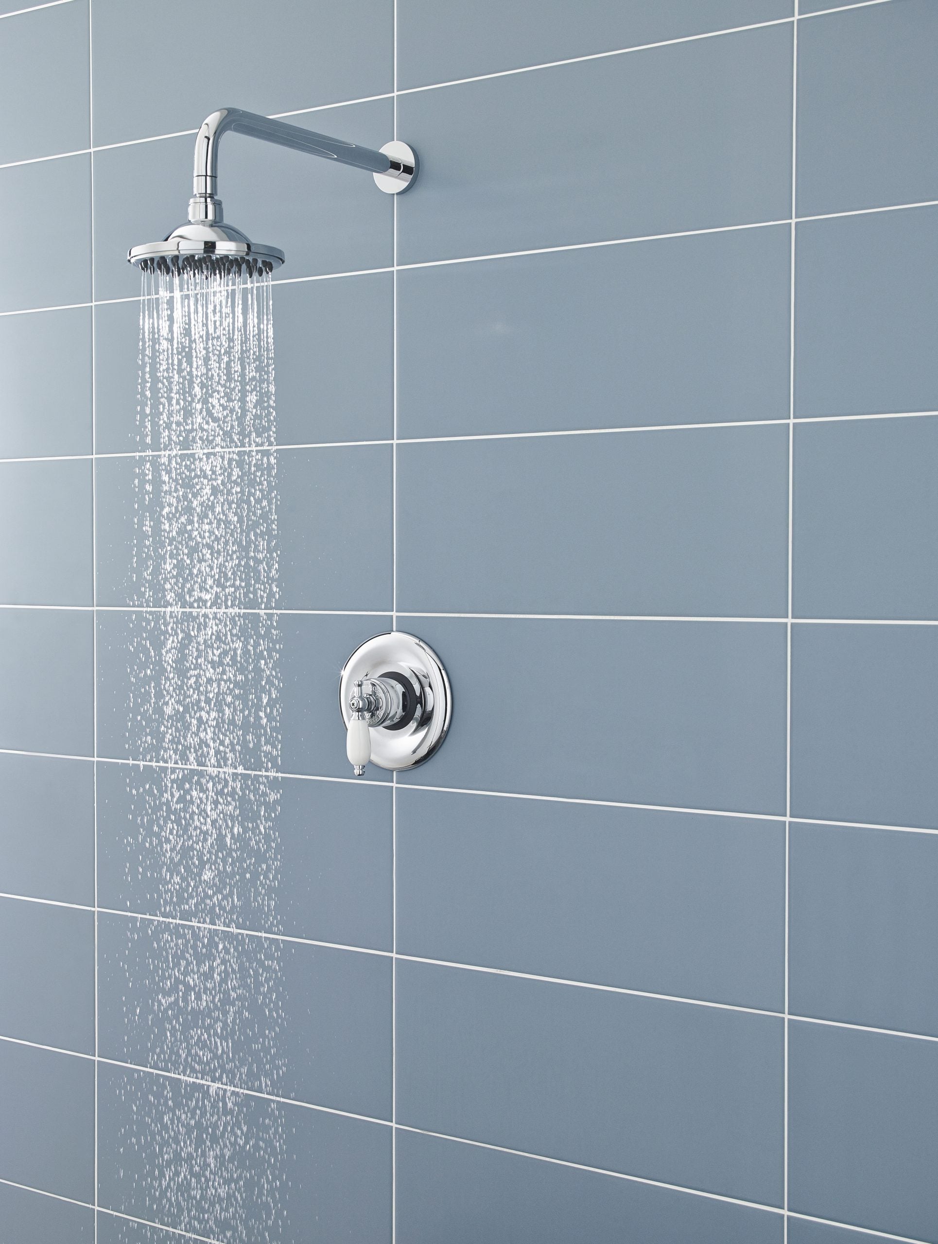 Shower head and control valve in a modern bathroom with blue tiles, chrome fixtures, and water flowing from the shower. Perfect for contemporary bathroom design and renovation ideas.