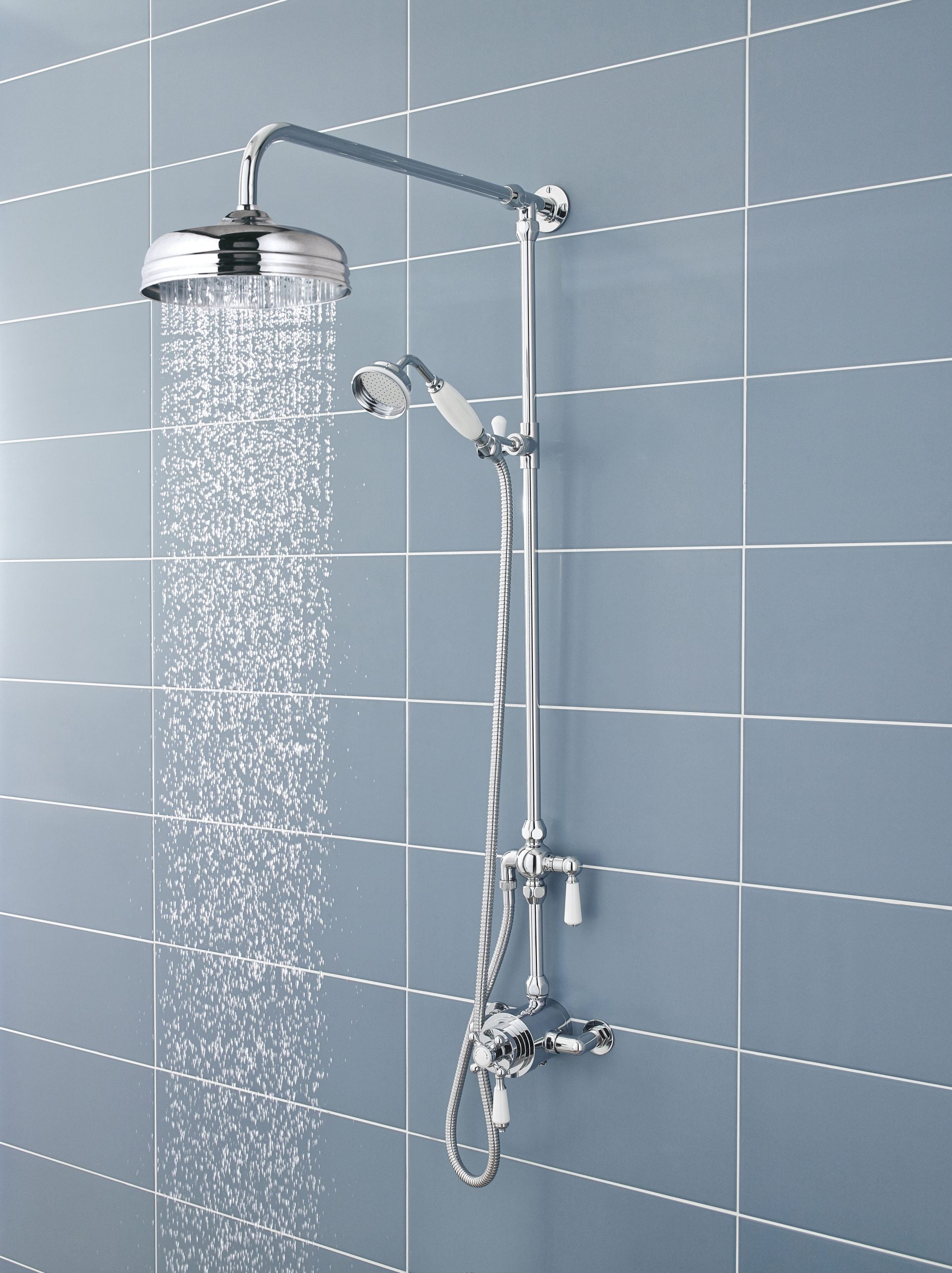 Polished chrome shower system with rainfall and handheld shower heads mounted on a blue tiled bathroom wall.