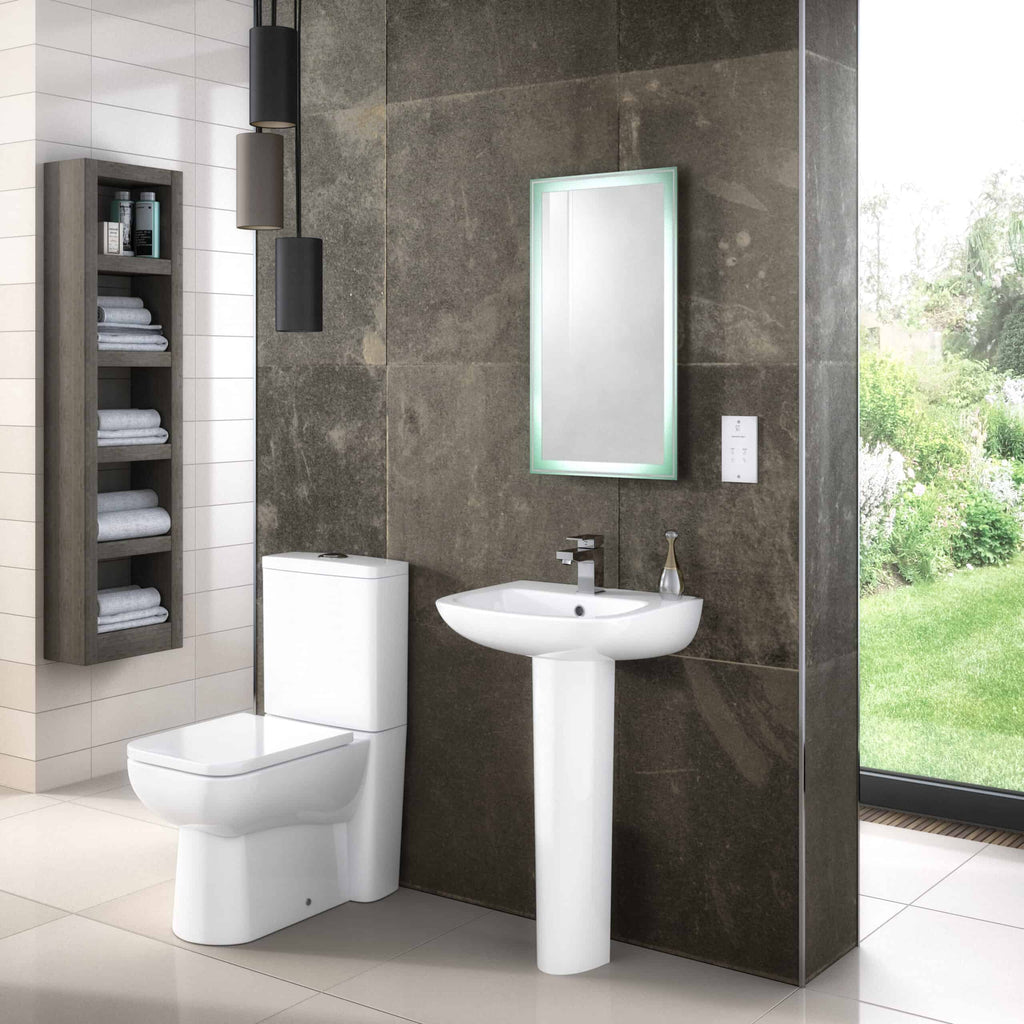 Sleek modern bathroom with white toilet, pedestal sink, illuminated mirror, grey wall tiles, and large glass window overlooking a lush garden. Stylish and functional bathroom design by Bubly Bathrooms.
