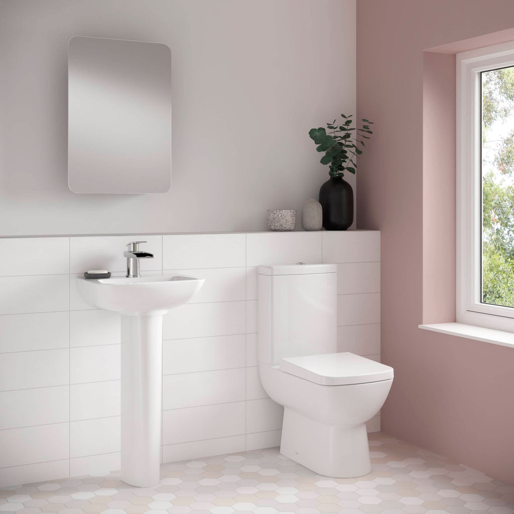 Minimalist bathroom with white sanitary ware, pedestal sink, modern toilet, and decorative vases in soft pink and neutral tones with a large window and natural light.