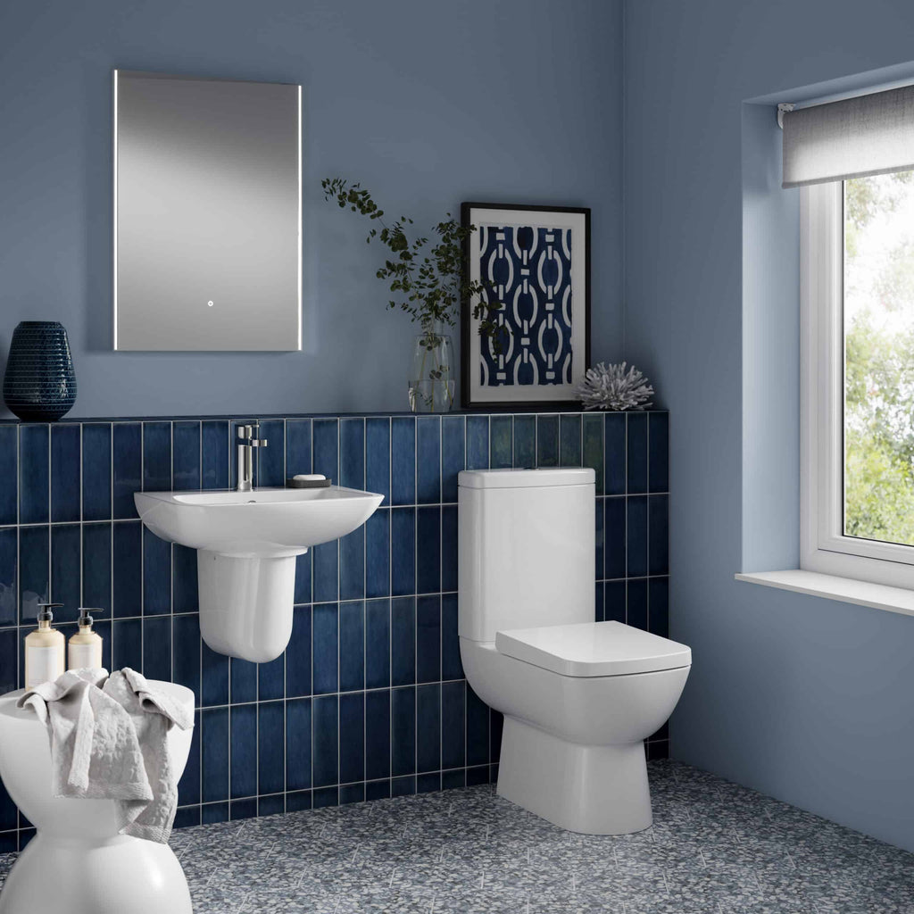 Modern white toilet and small wall-mounted sink in a contemporary blue-tiled bathroom with natural light from a window.