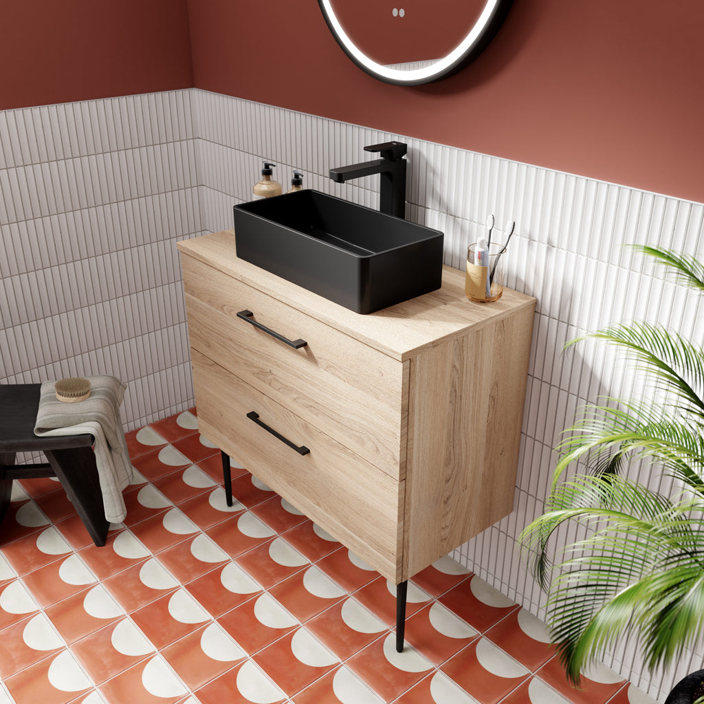 Sleek black rectangular bathroom sink on a light wood vanity unit with modern black handles, set against white tiled walls with a pink accent wall for a contemporary bathroom design.