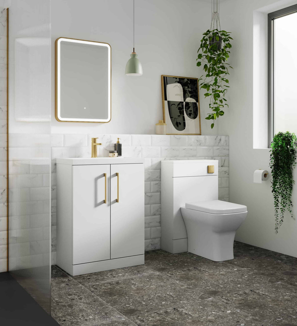Sleek modern white bathroom vanity with gold handles, gold faucet, and matching toilet, complemented by marble tiles and lush green plants, creating a stylish and contemporary bubble bath space.
