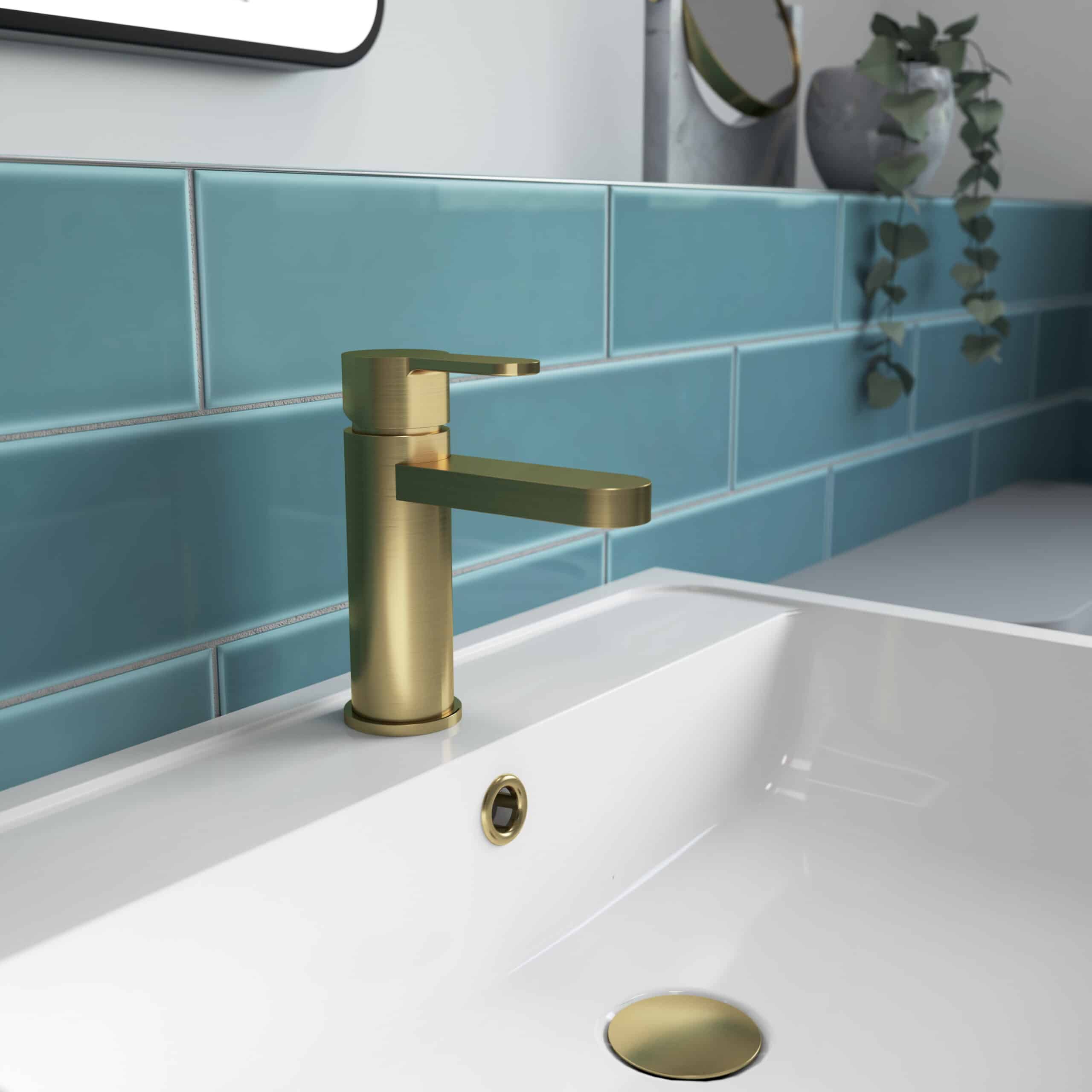 Brass bathroom faucet with modern design, mounted on a white sink against a backdrop of blue subway tiles and decorative plants, showcasing contemporary Bubly Bathrooms styling.
