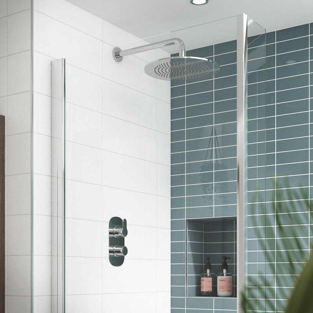 Shower-head and controls in modern shower enclosure with white and blue tiled walls, minimalist bathroom design, chrome fixtures, glass partition, and built-in niche with bottles, contemporary shower room design.
