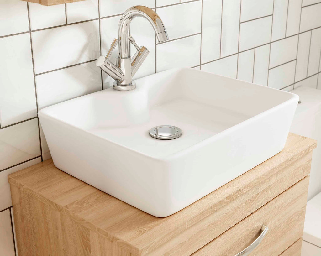 Sleek white ceramic bathroom sink with modern chrome faucet mounted on a wooden vanity, surrounded by white tiled walls, ideal for contemporary bathroom designs.