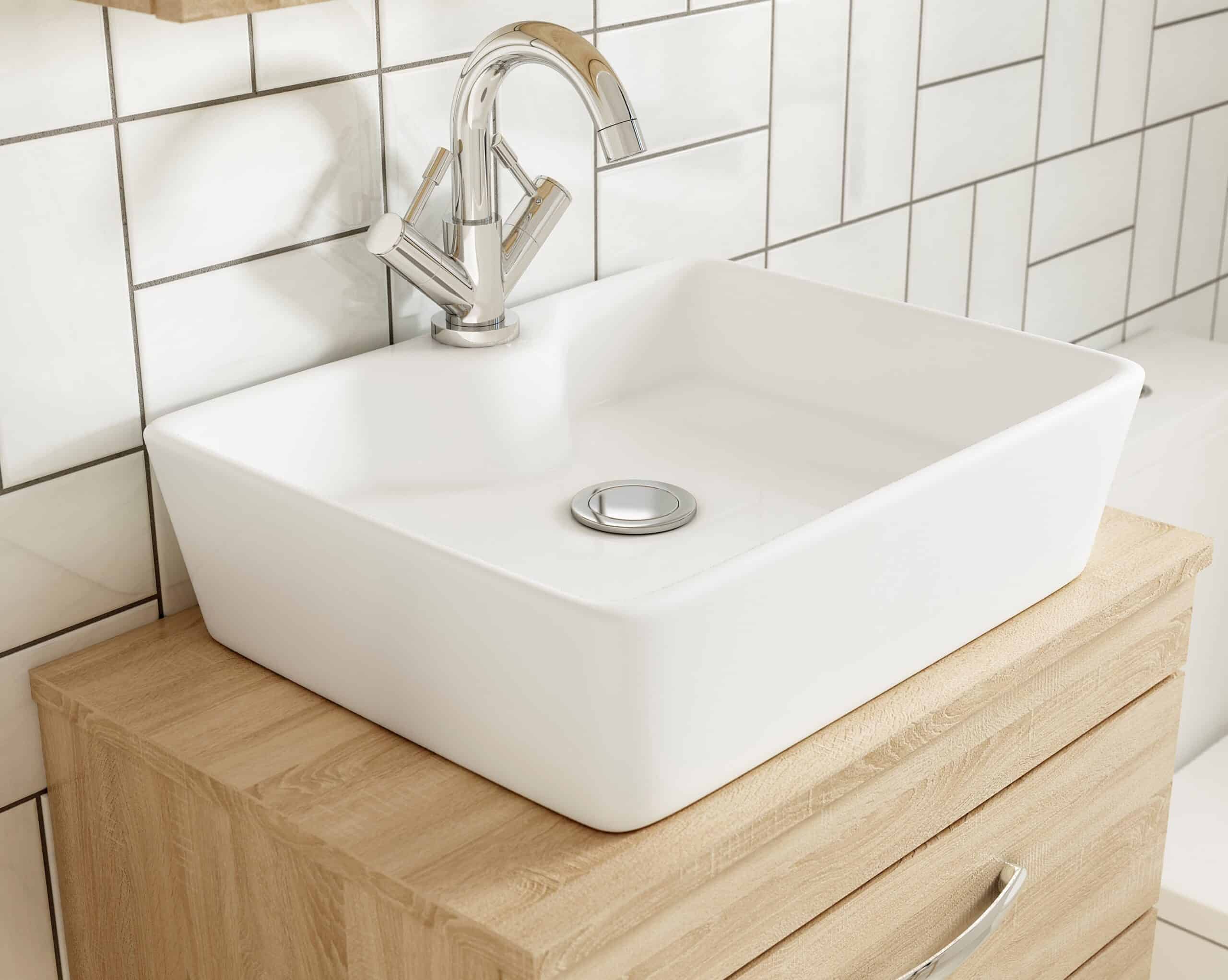 Sleek white ceramic bathroom sink with modern chrome faucet mounted on a wooden vanity, surrounded by white tiled walls, ideal for contemporary bathroom designs.