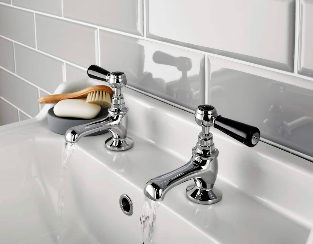 Polished chrome bathroom taps with black handles on a white ceramic sink, modern bathroom fixtures, and accessories for a stylish and functional bathroom design.