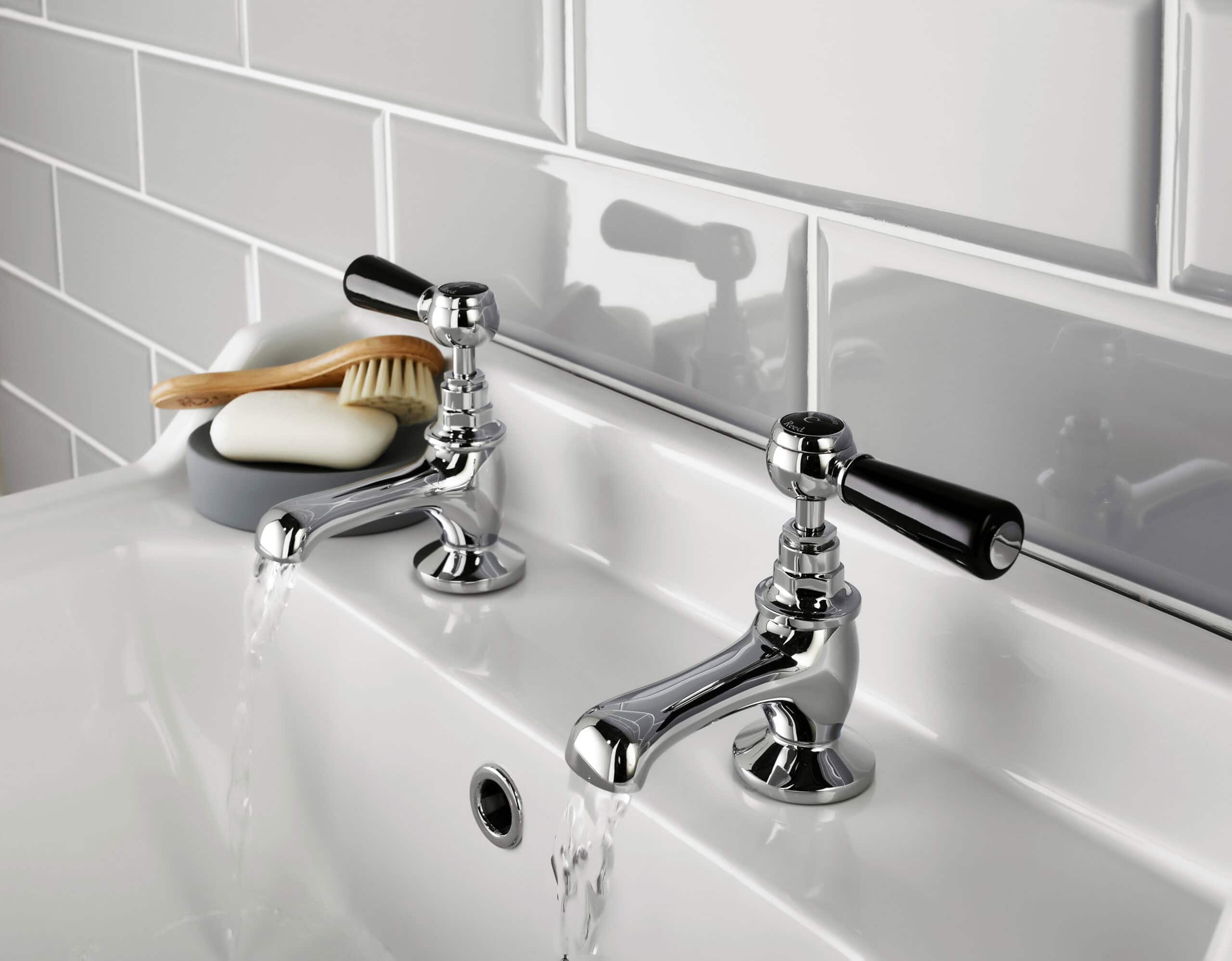 Polished chrome bathroom taps with black handles on a white ceramic sink, modern bathroom fixtures, and accessories for a stylish and functional bathroom design.