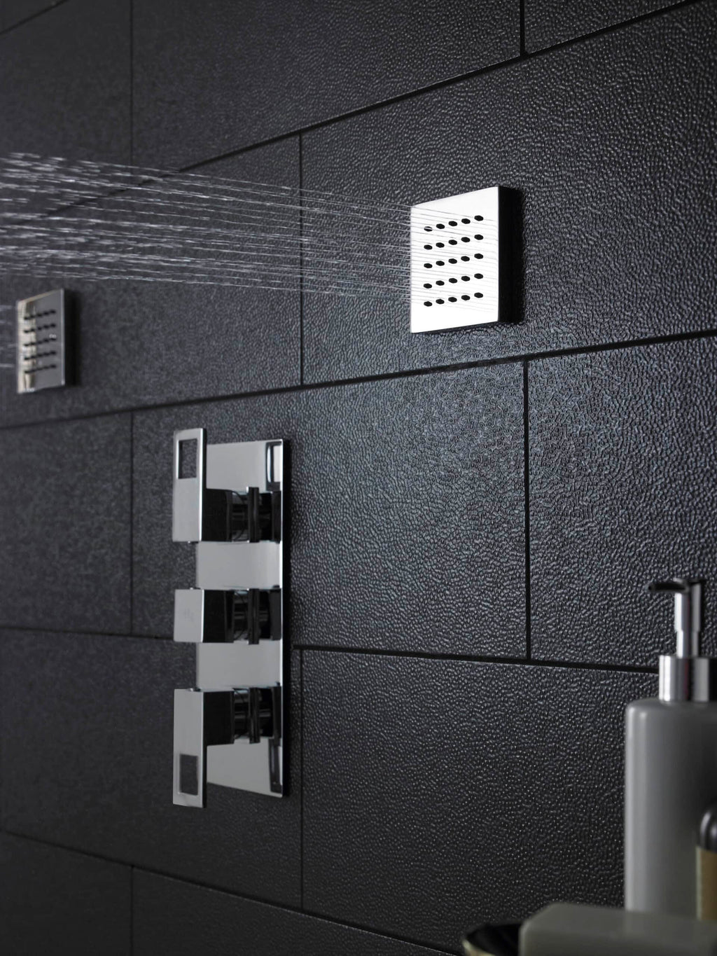 Sleek modern shower with chrome fixtures and black textured tile walls, showcasing stylish bathroom design.