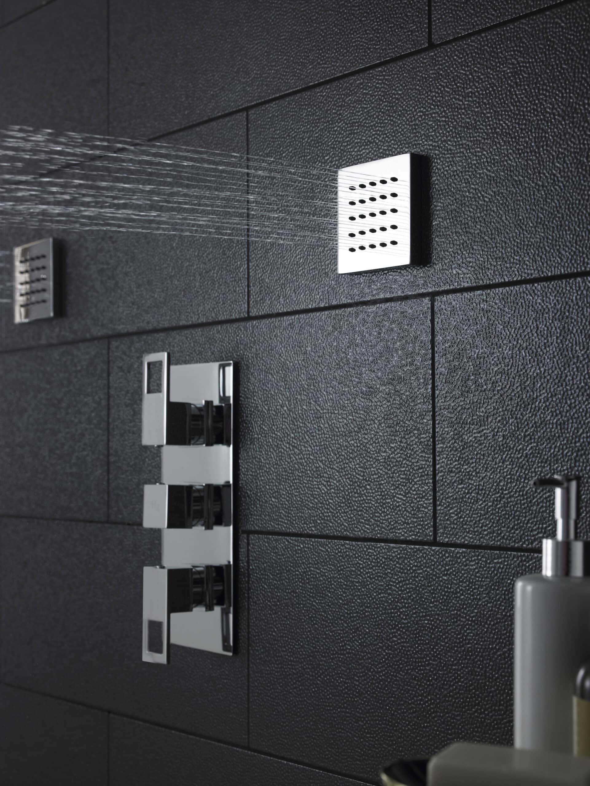 Sleek modern shower with chrome fixtures and black textured tile walls, showcasing stylish bathroom design.