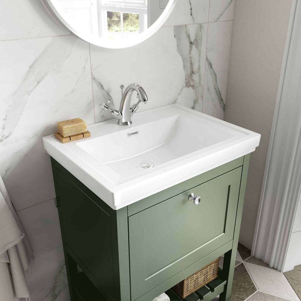 Rustic bathroom vanity with white ceramic sink and green wooden cabinet, featuring modern chrome tap, set against marble tiled wall with a round mirror for a stylish bathroom look.