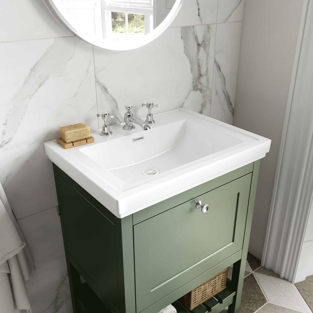 Vintage green bathroom vanity with a white ceramic sink and chrome taps, set against marble wall tiles; elegant and functional bathroom decor.