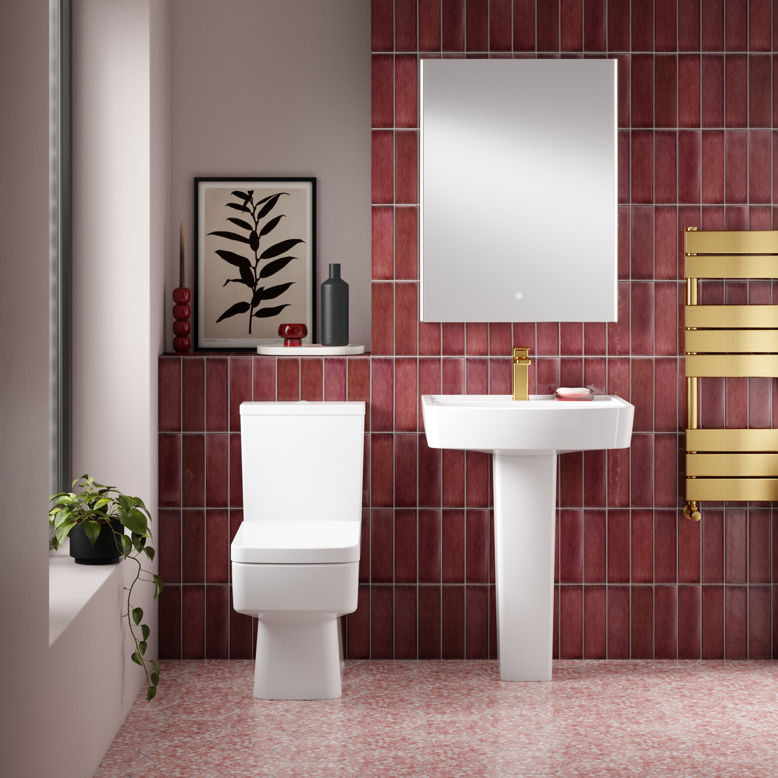 Modern bathroom with white toilet and pedestal sink, red tiled walls, gold heated towel rail, and decorative accessories, creating a stylish and functional space.