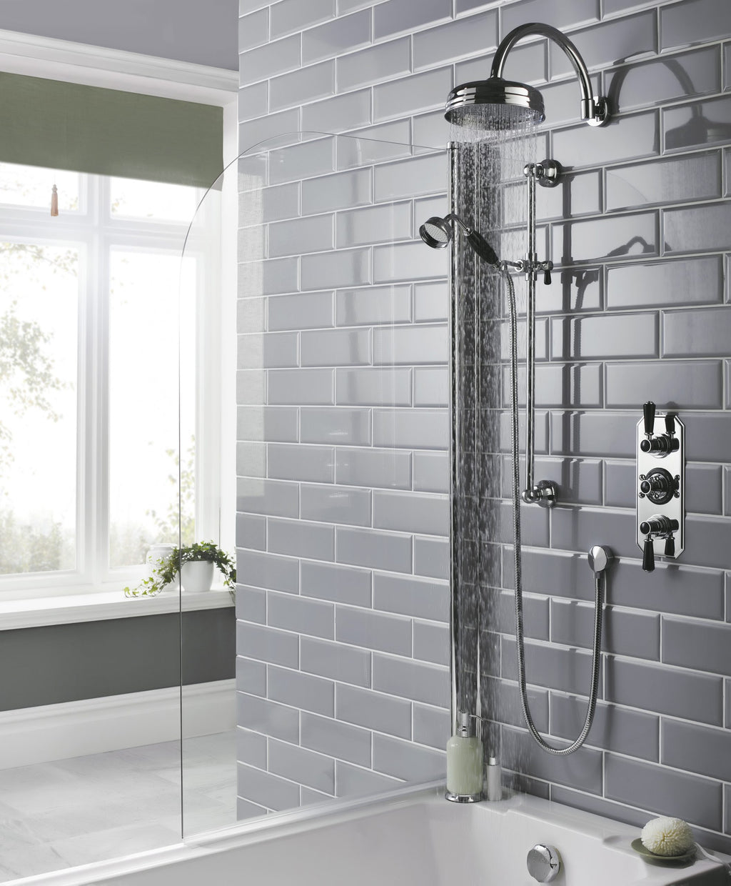 Showerhead and control panel in a modern bathroom with grey tiled walls and large window, showcasing sleek bathroom fixtures and contemporary design elements.