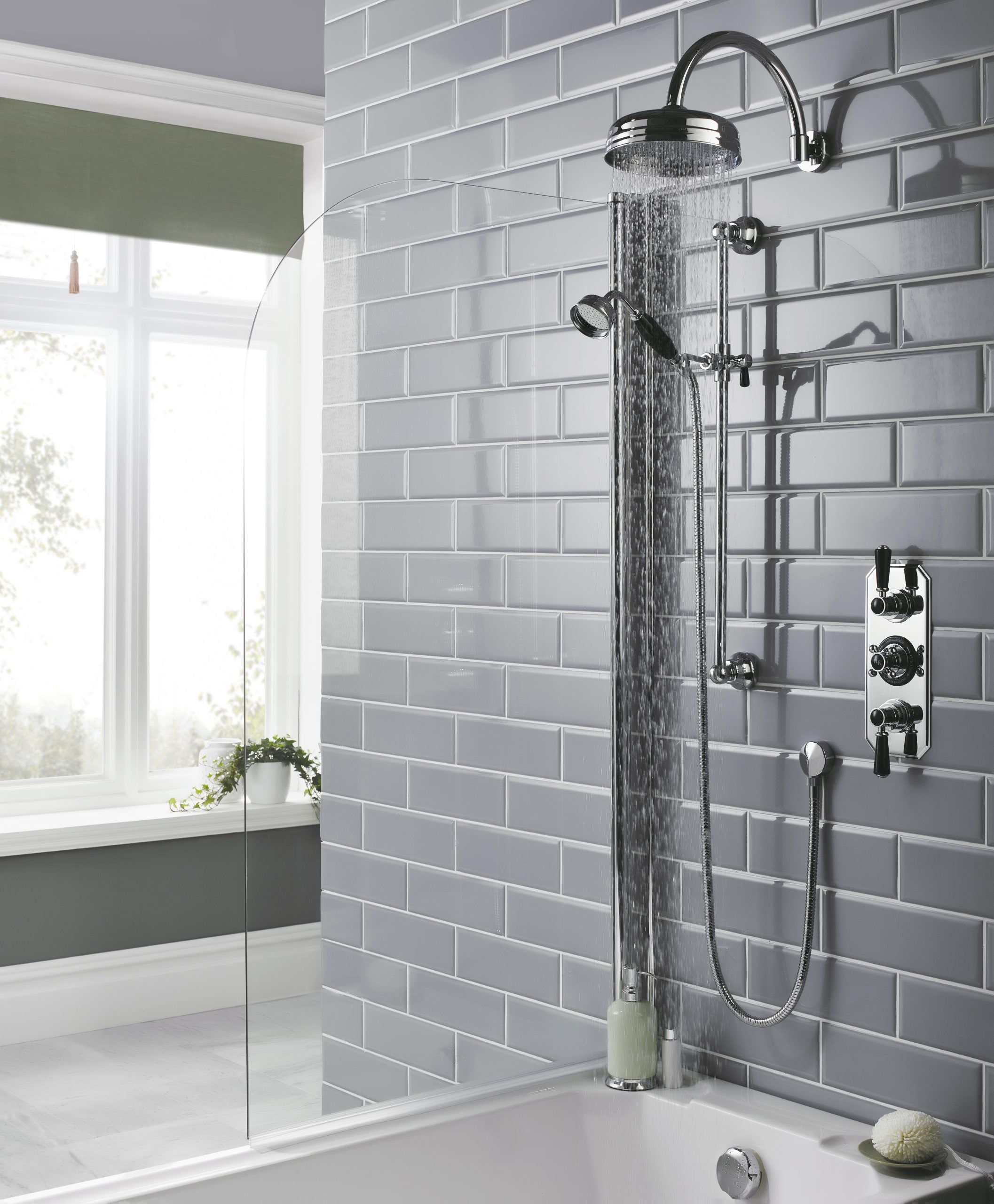 Showerhead and control panel in a modern bathroom with grey tiled walls and large window, showcasing sleek bathroom fixtures and contemporary design elements.