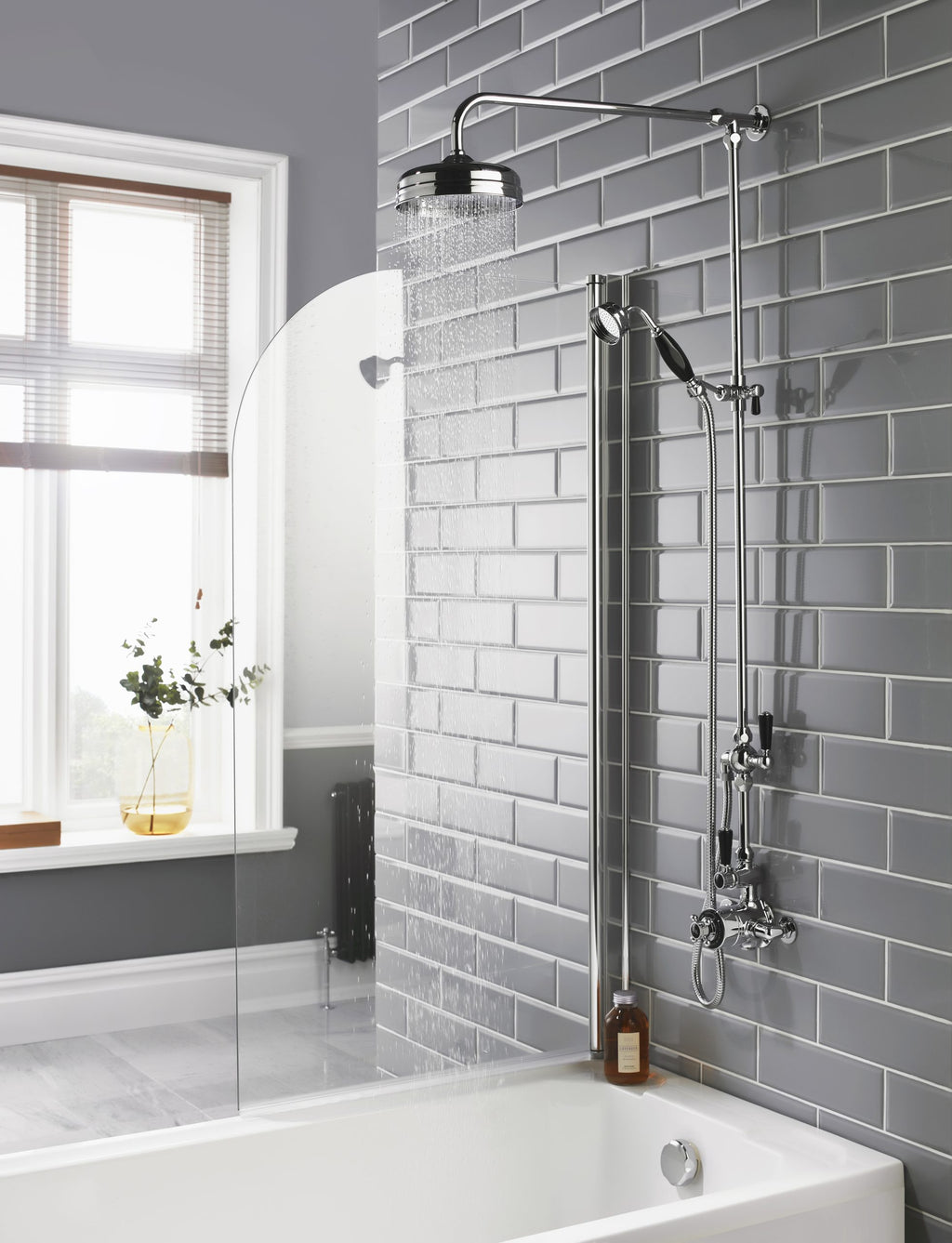 Modern grey tile bathroom shower setup with overhead and handheld shower heads, glass shower screen, natural light from window, minimalist design, and stylish accessories.
