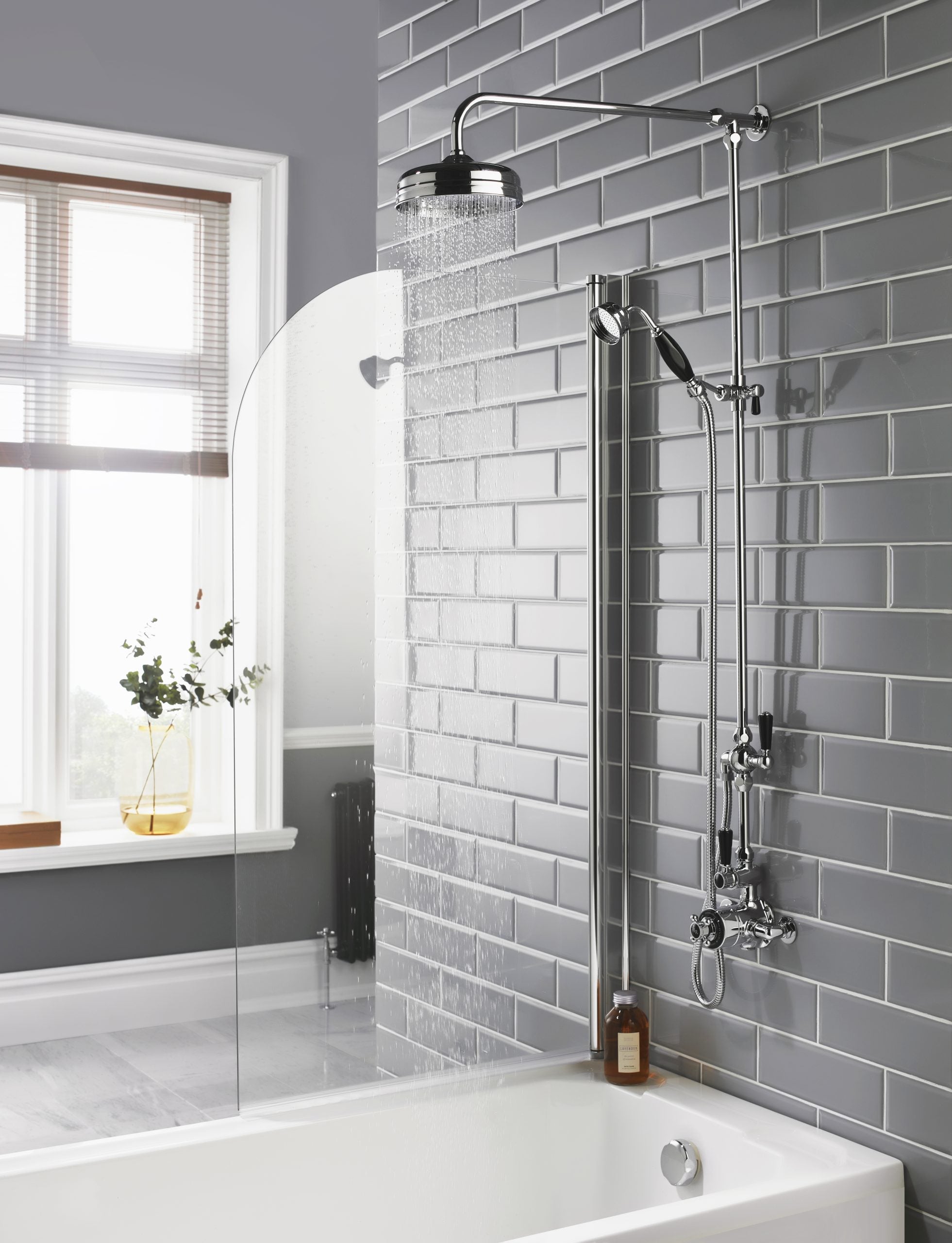 Modern grey tile bathroom shower setup with overhead and handheld shower heads, glass shower screen, natural light from window, minimalist design, and stylish accessories.