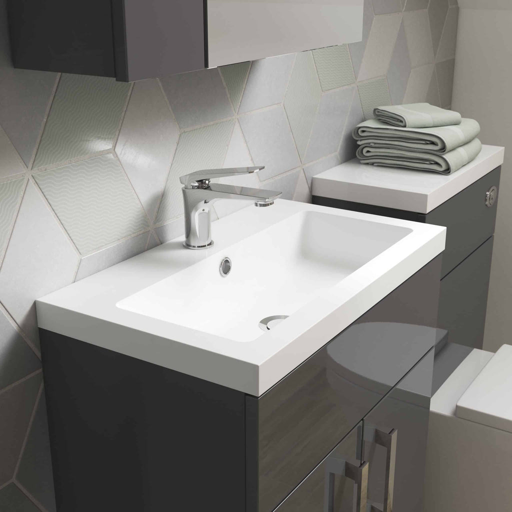 Modern bathroom vanity with white sink and chrome faucet, grey cabinetry, tiled wall, and neatly folded towels on countertop, showcasing contemporary bathroom design.