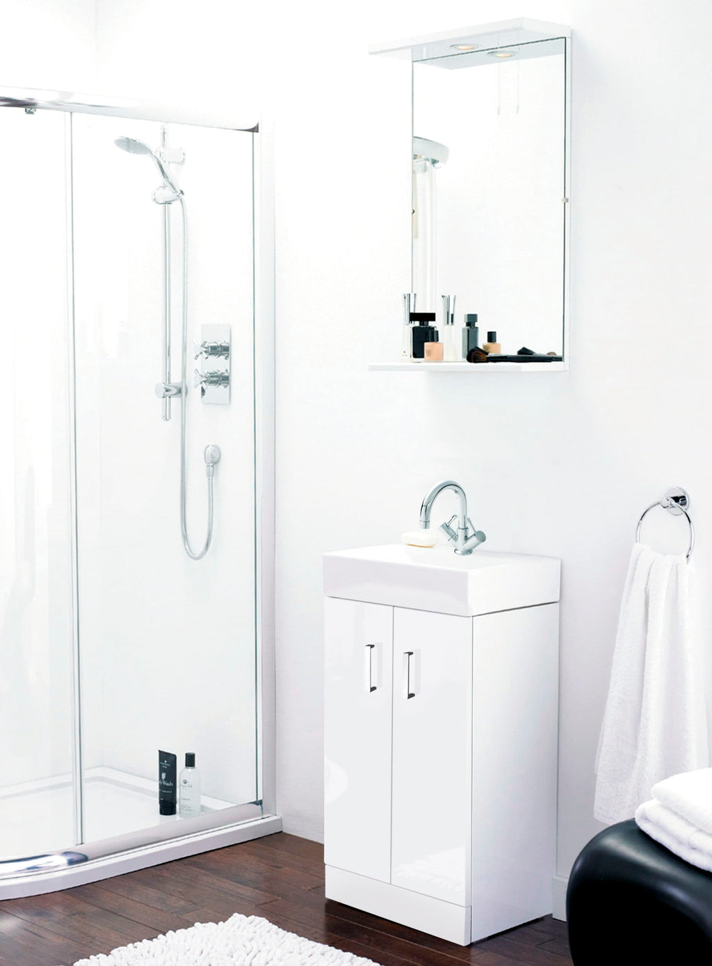 Shower enclosure with chrome fixtures, white bathroom vanity with sink, wall mirror cabinet, white towel on towel ring, and dark wooden flooring in modern minimalist bathroom.