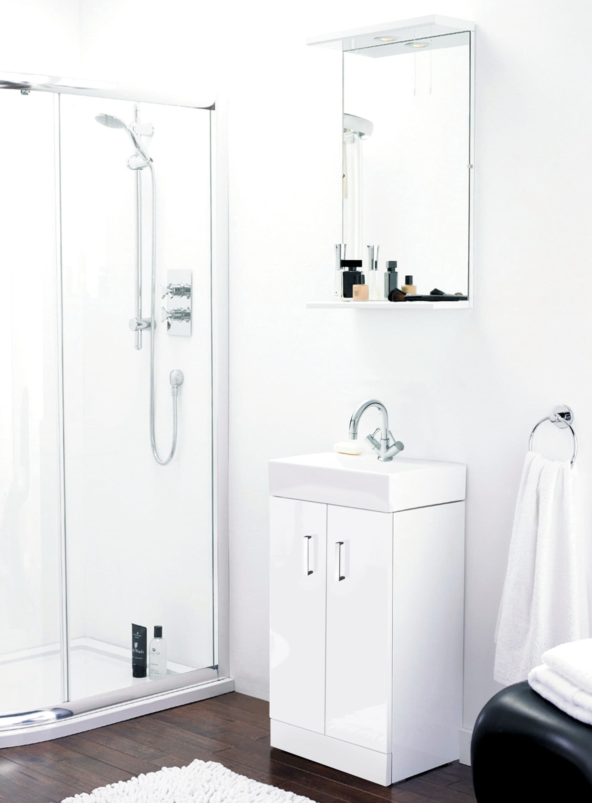 Shower enclosure with chrome fixtures, white bathroom vanity with sink, wall mirror cabinet, white towel on towel ring, and dark wooden flooring in modern minimalist bathroom.