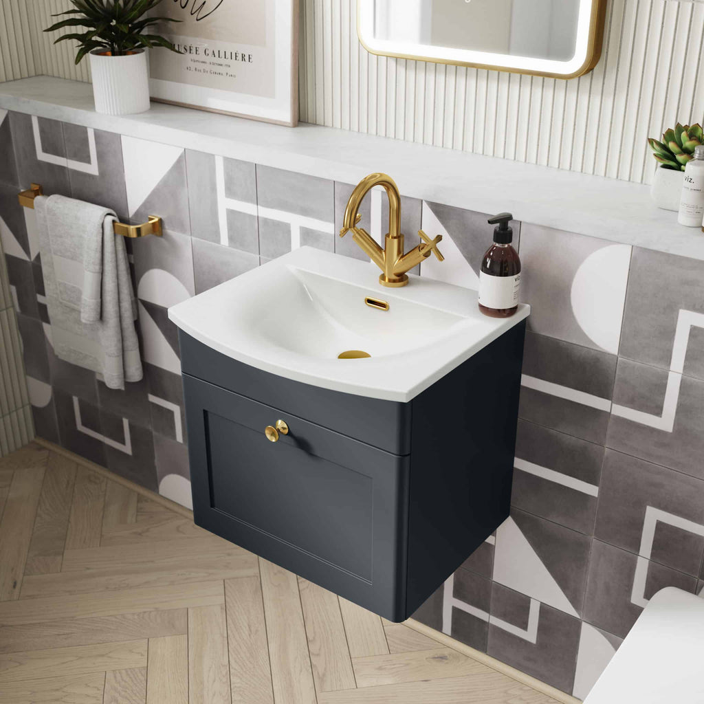 Sleek navy bathroom vanity with white ceramic sink and gold fixtures, set against modern geometric tiled wall, featuring a brass towel rail and decorative elements; stylish bathroom design.