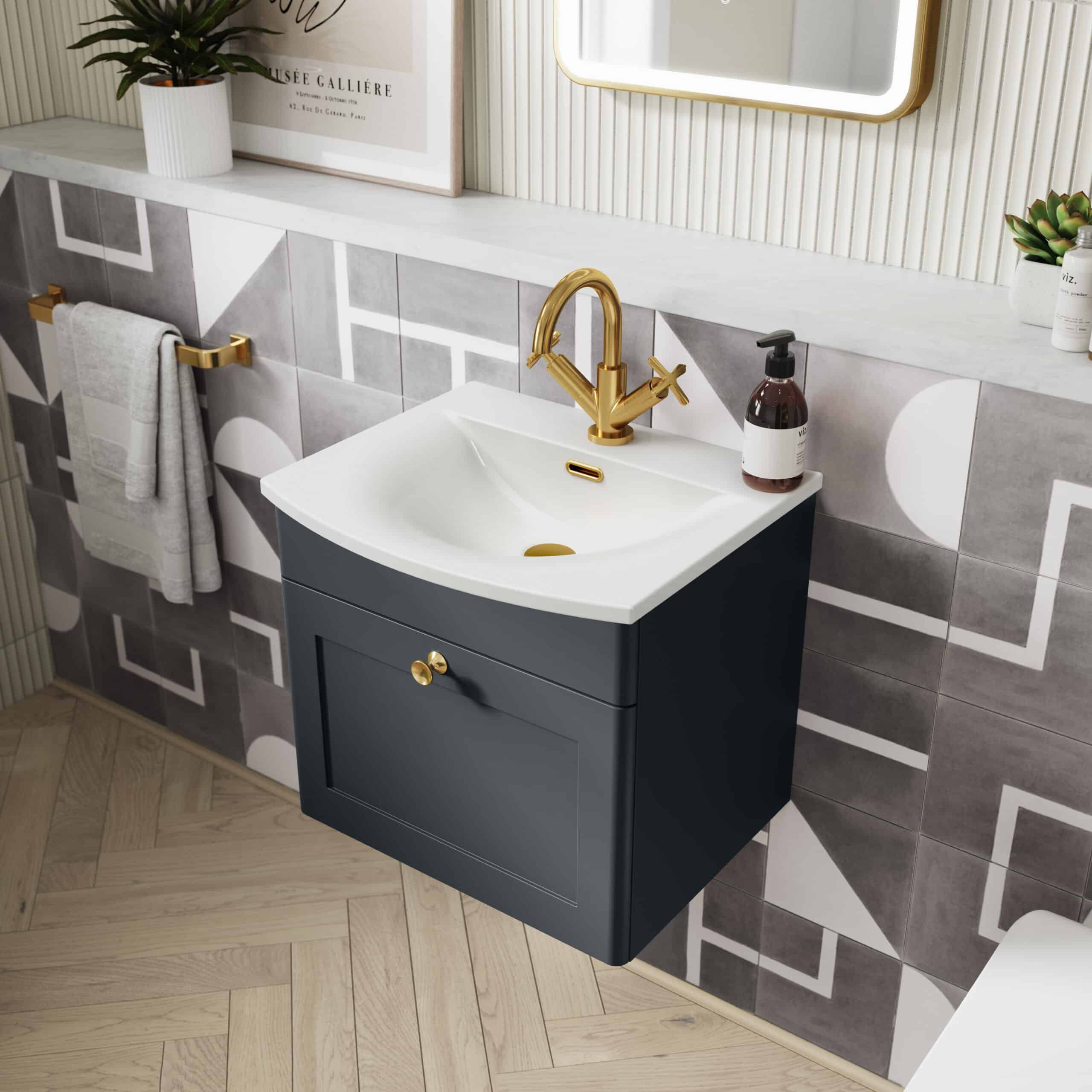 Sleek navy bathroom vanity with white ceramic sink and gold fixtures, set against modern geometric tiled wall, featuring a brass towel rail and decorative elements; stylish bathroom design.