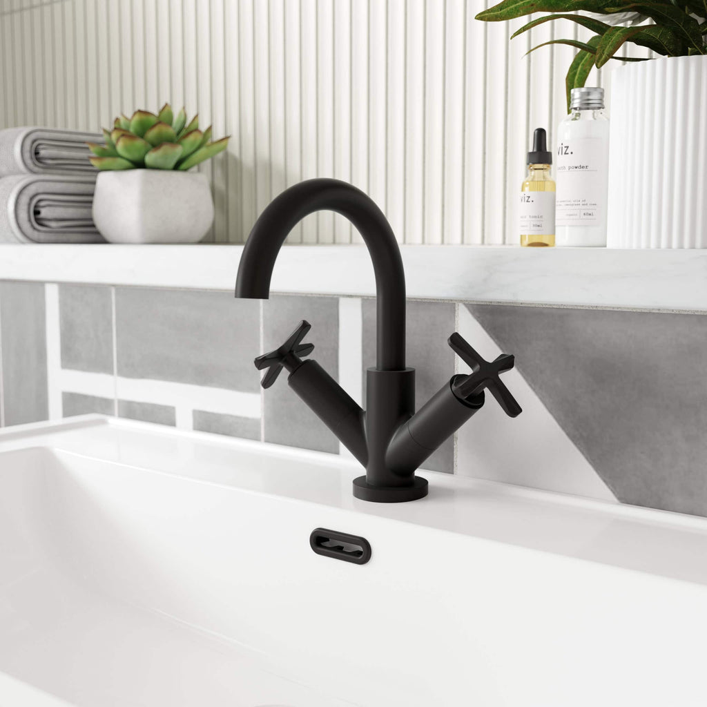 Sleek black kitchen or bathroom tap with dual handles on a modern white sink, surrounded by minimalist decor including plants, towels, and skincare bottles for contemporary bathroom design.