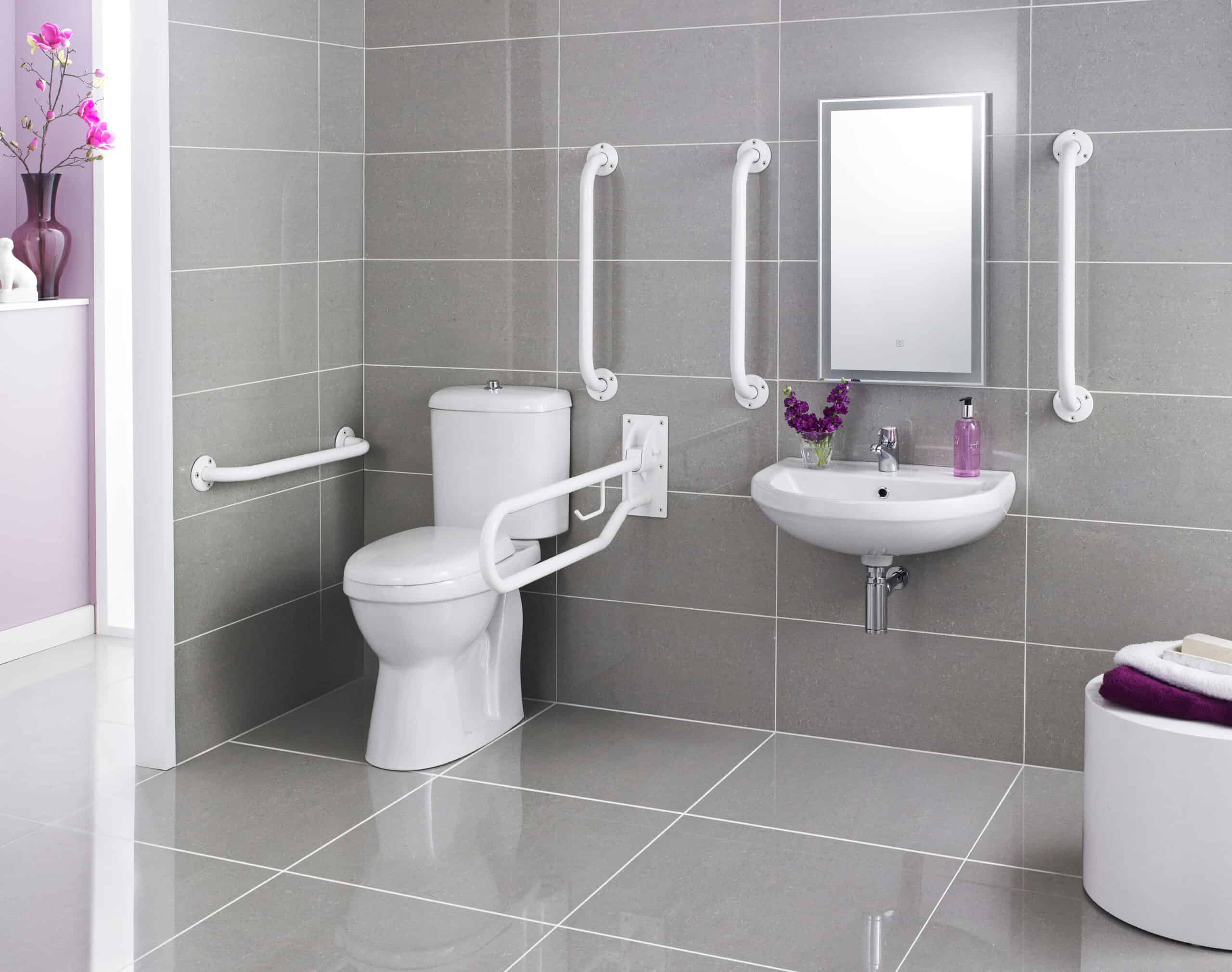 Anti-slip bathroom with accessible toilet and wall-mounted sink, featuring white grab bars for safety, grey tiled walls, and a sleek mirror; designed for accessible bathing and toilet use.