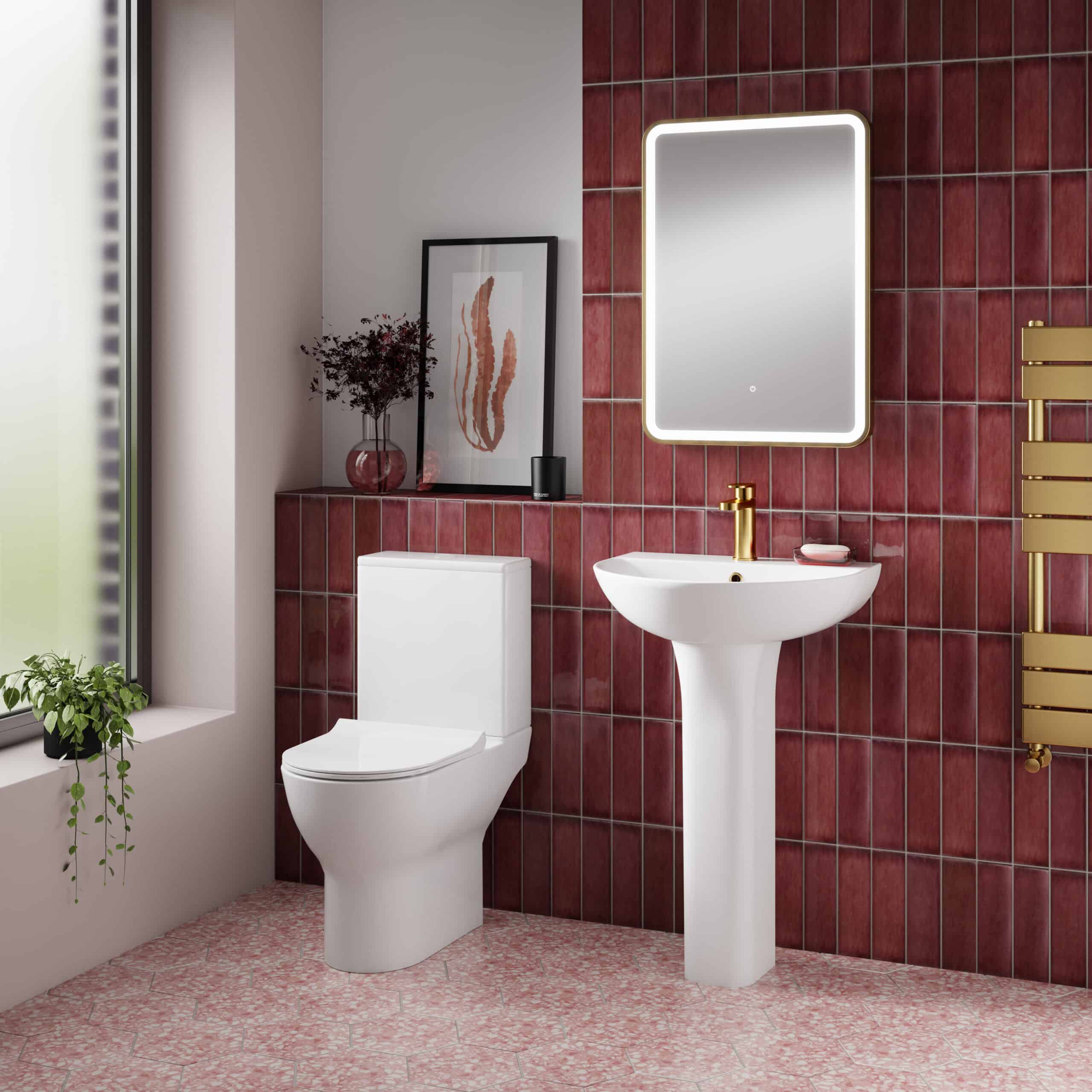 Modern bathroom with white toilet, pedestal sink, illuminated mirror, red tiled wall, and brass fixtures, perfect for contemporary bathroom bath renovation ideas.