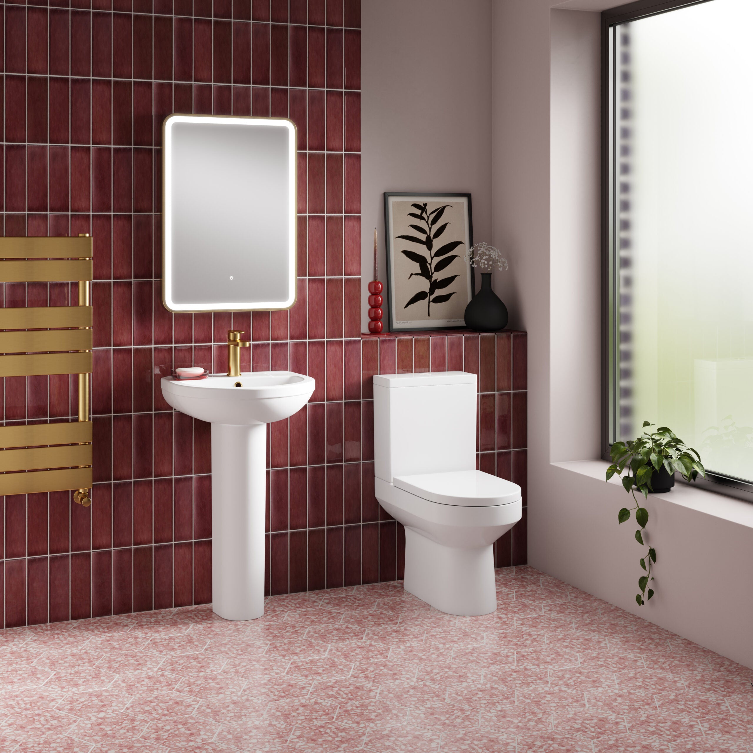 Modern bathroom with white toilet and pedestal sink, black framed mirror, red tiled wall, pink mosaic floor, decorative plants, and natural light from large window, showcasing contemporary bathroom design.