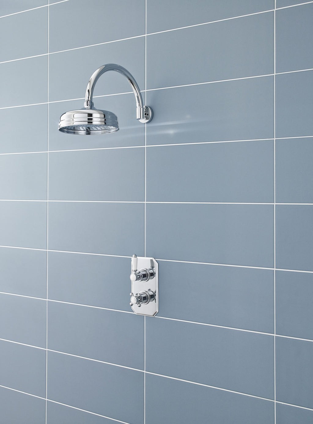 Polished chrome shower head and control valve on blue tiled wall, modern bathroom fixtures for a stylish shower setup.