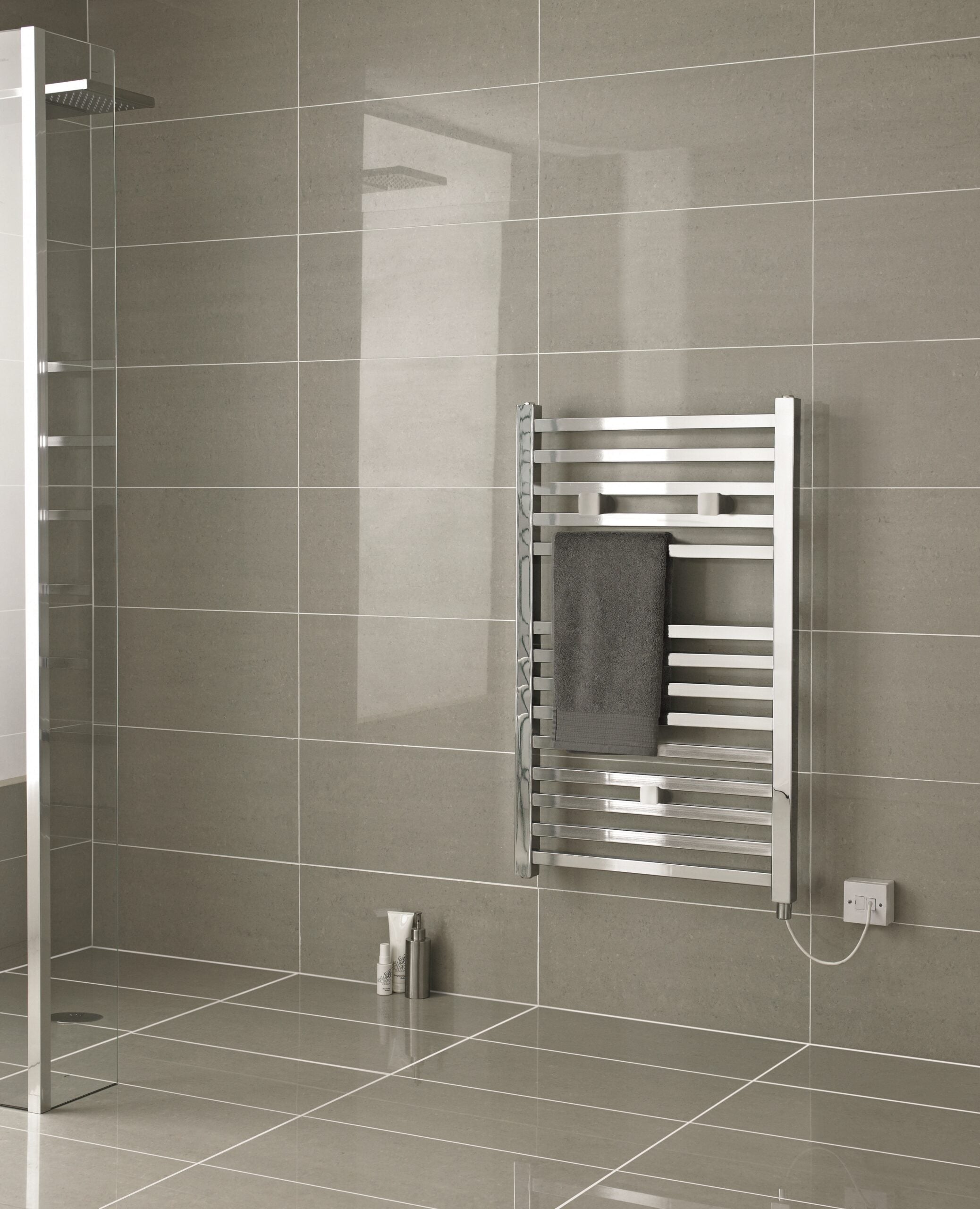 Modern stainless steel towel radiator in a sleek bathroom with large beige tiles and minimalist design.
