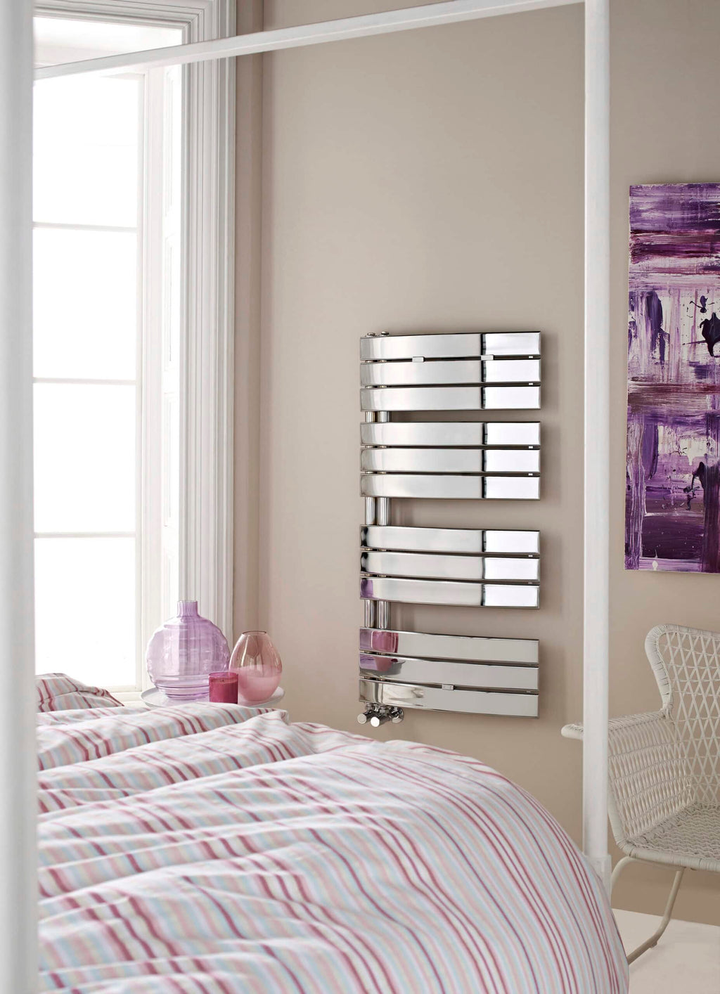 Sleek modern chrome towel radiator in a contemporary bathroom with pastel-coloured bedding and decorative pink vases.