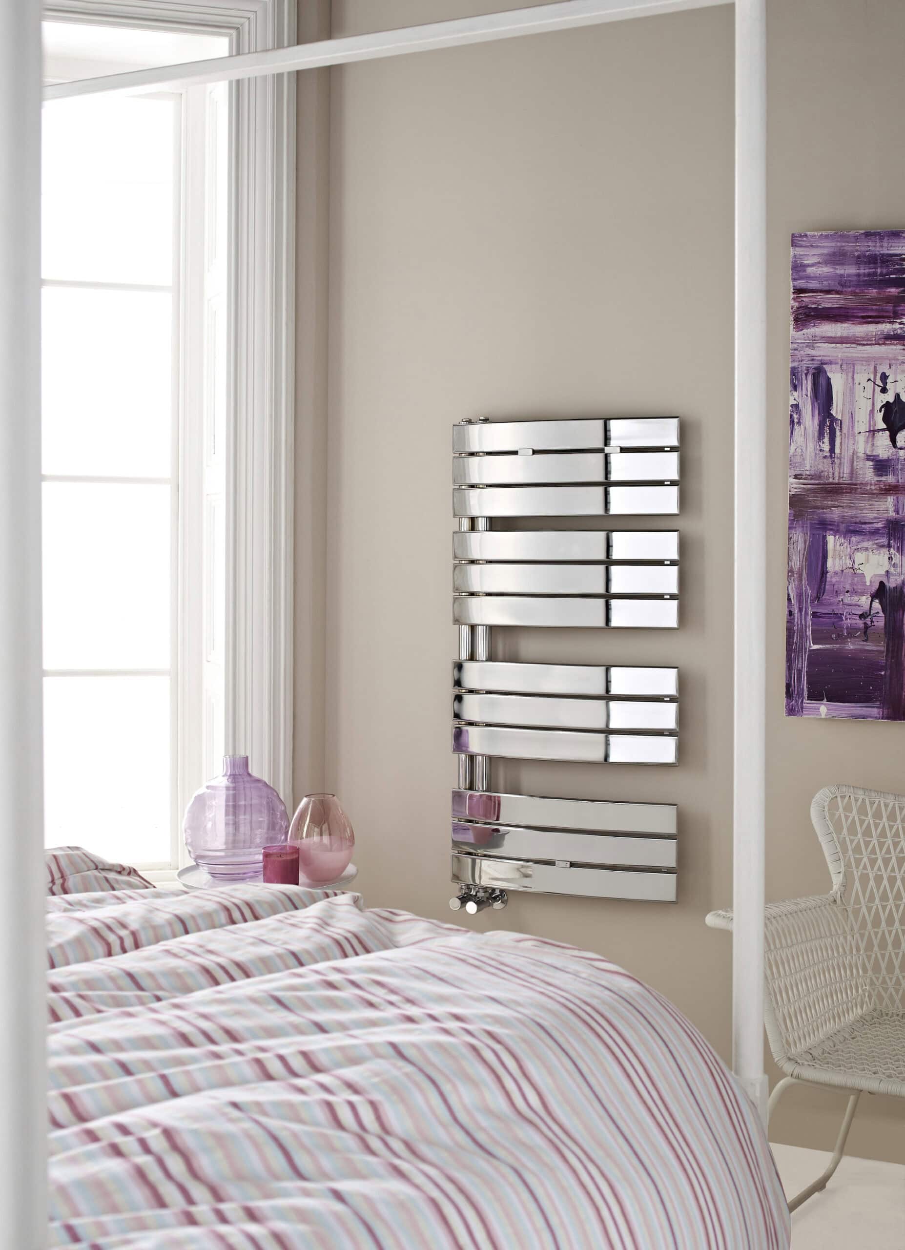 Sleek modern chrome towel radiator in a contemporary bathroom with pastel-coloured bedding and decorative pink vases.