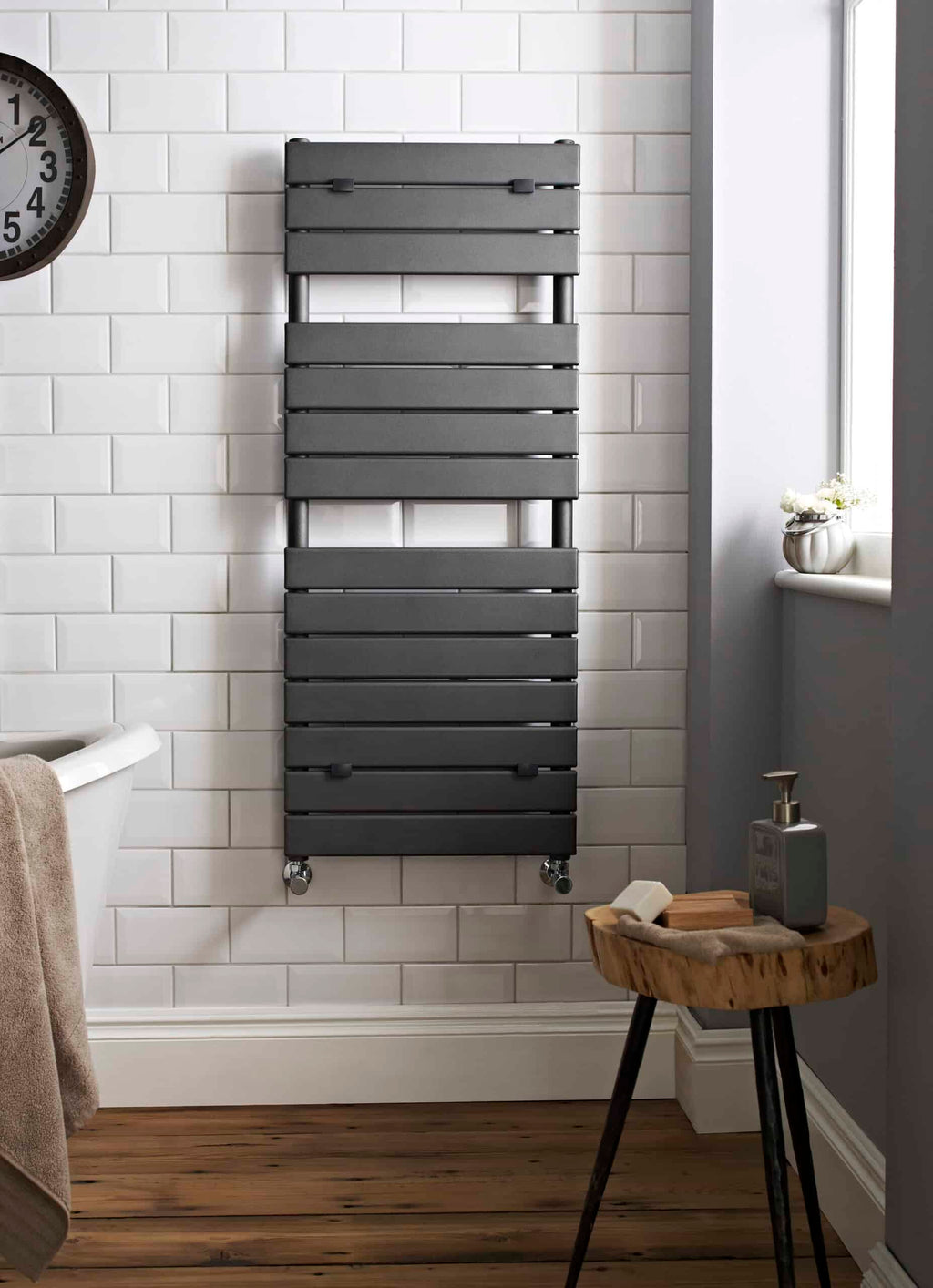 Sleek black towel radiator mounted on white tiled bathroom wall with wooden floor and window, ideal for modern bathroom heating and towel drying.