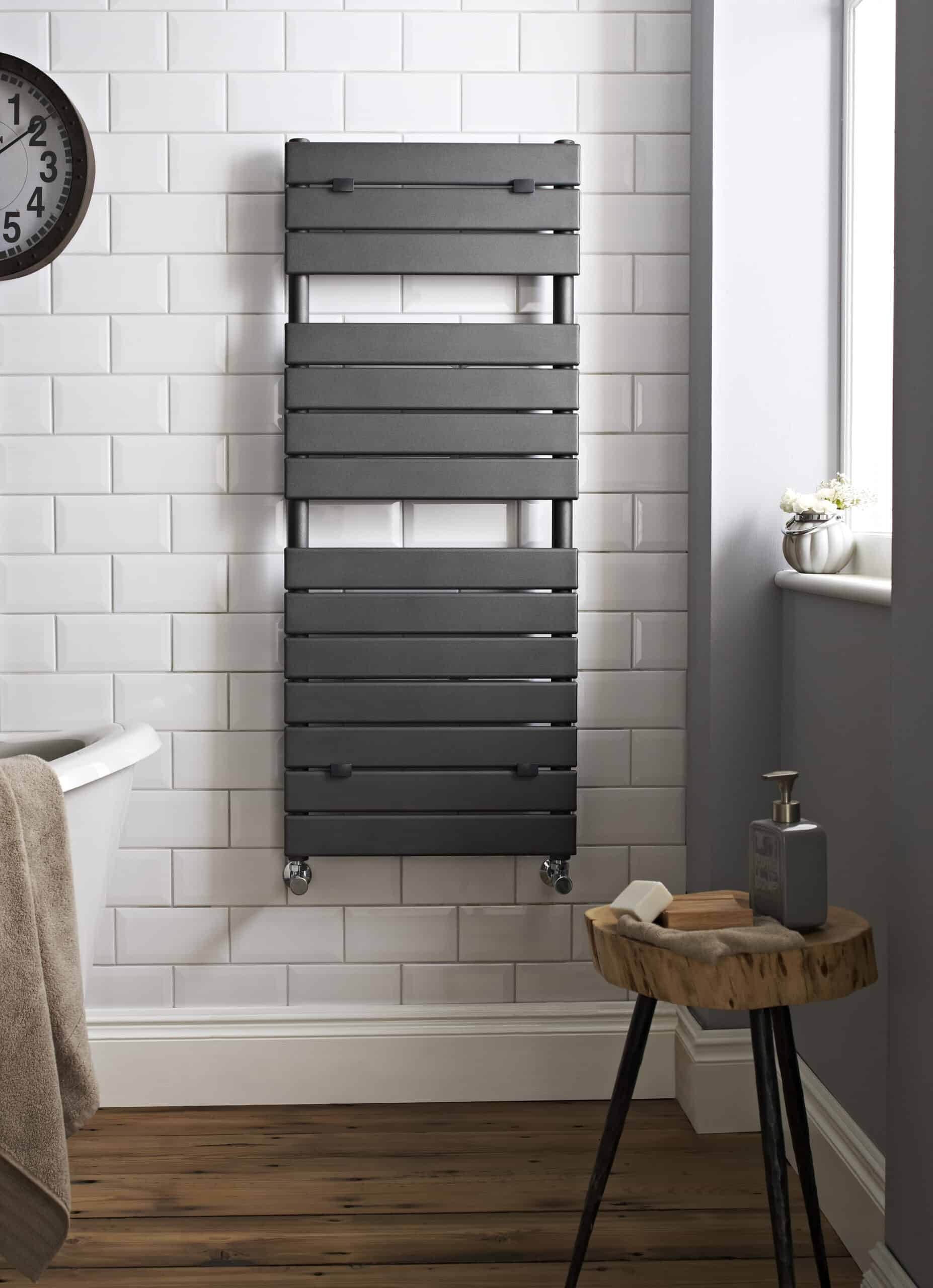 Sleek black towel radiator mounted on white tiled bathroom wall with wooden floor and window, ideal for modern bathroom heating and towel drying.