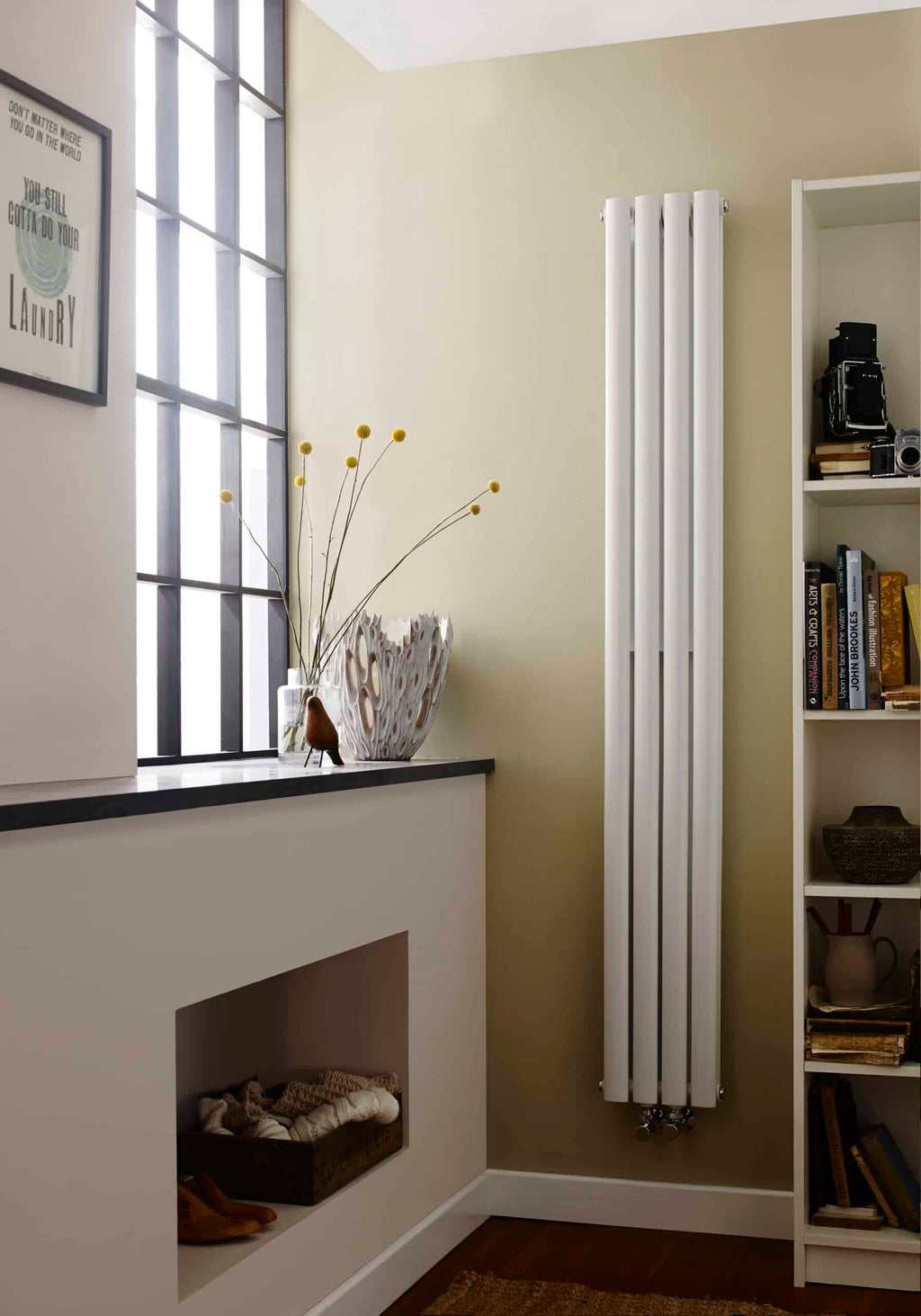 Modern vertical white radiator in a stylish bathroom or living space, paired with a bookshelves and decorative vase, providing functional heating and aesthetic appeal.