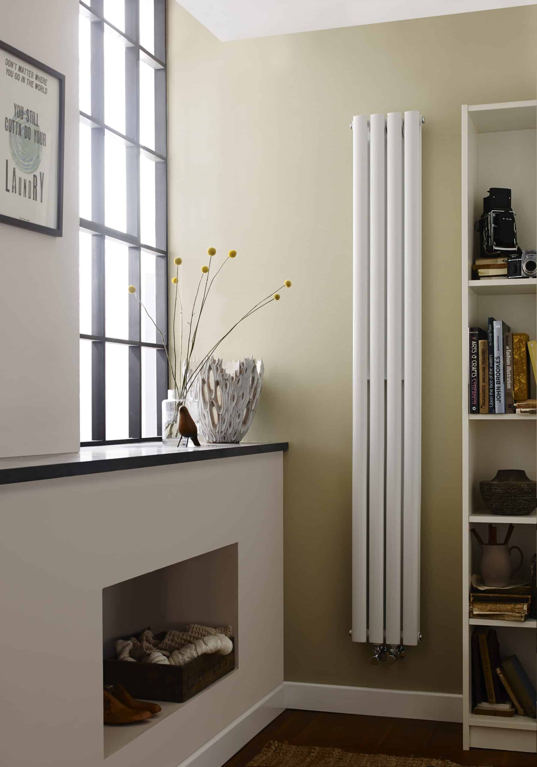 Modern vertical white radiator in a stylish bathroom or living space, paired with a bookshelves and decorative vase, providing functional heating and aesthetic appeal.