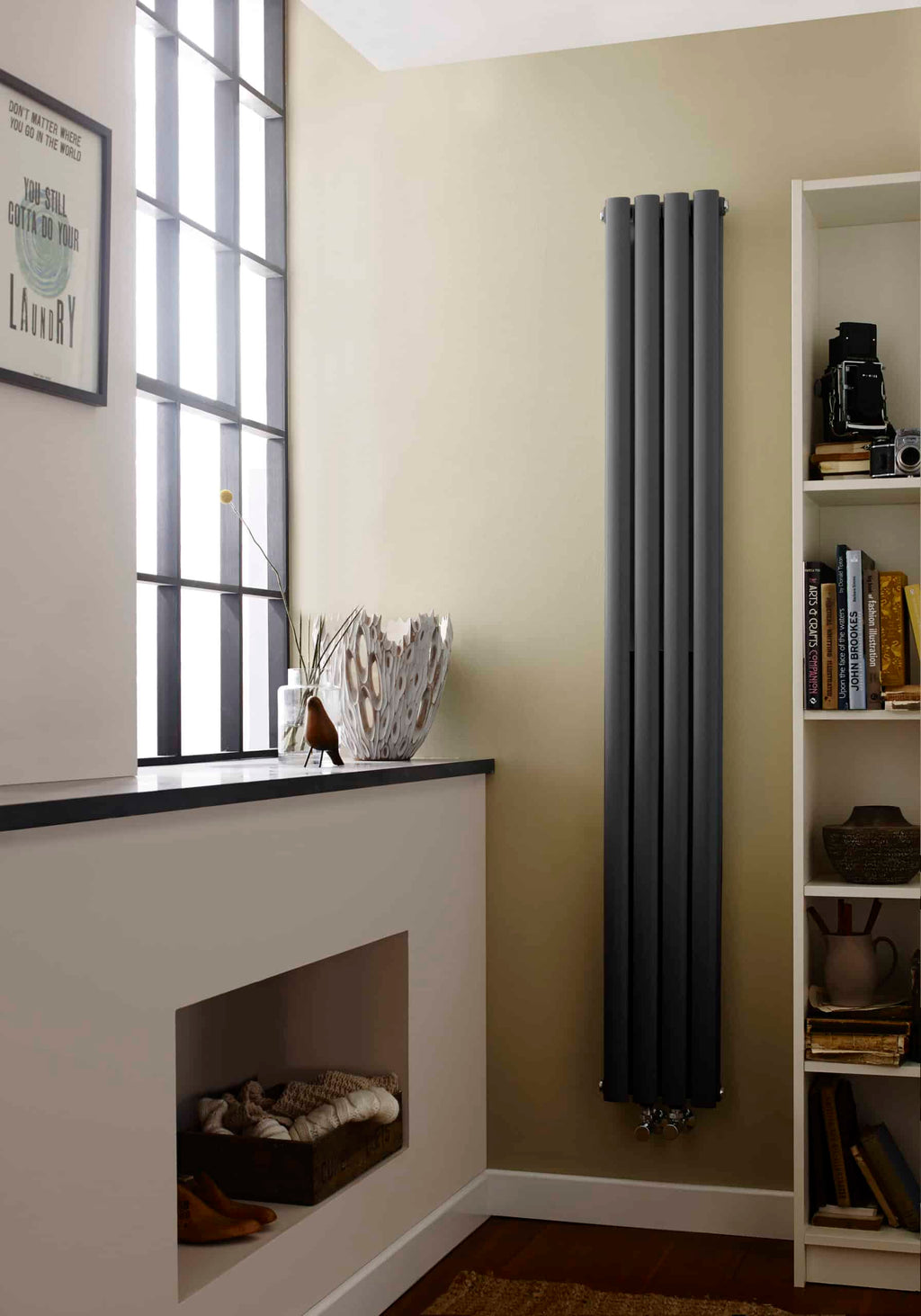 Sleek black vertical radiator in a modern bathroom with a window ledge decorated with ornaments and a white bookshelf, showcasing contemporary bathroom design and effective space heating solutions.
