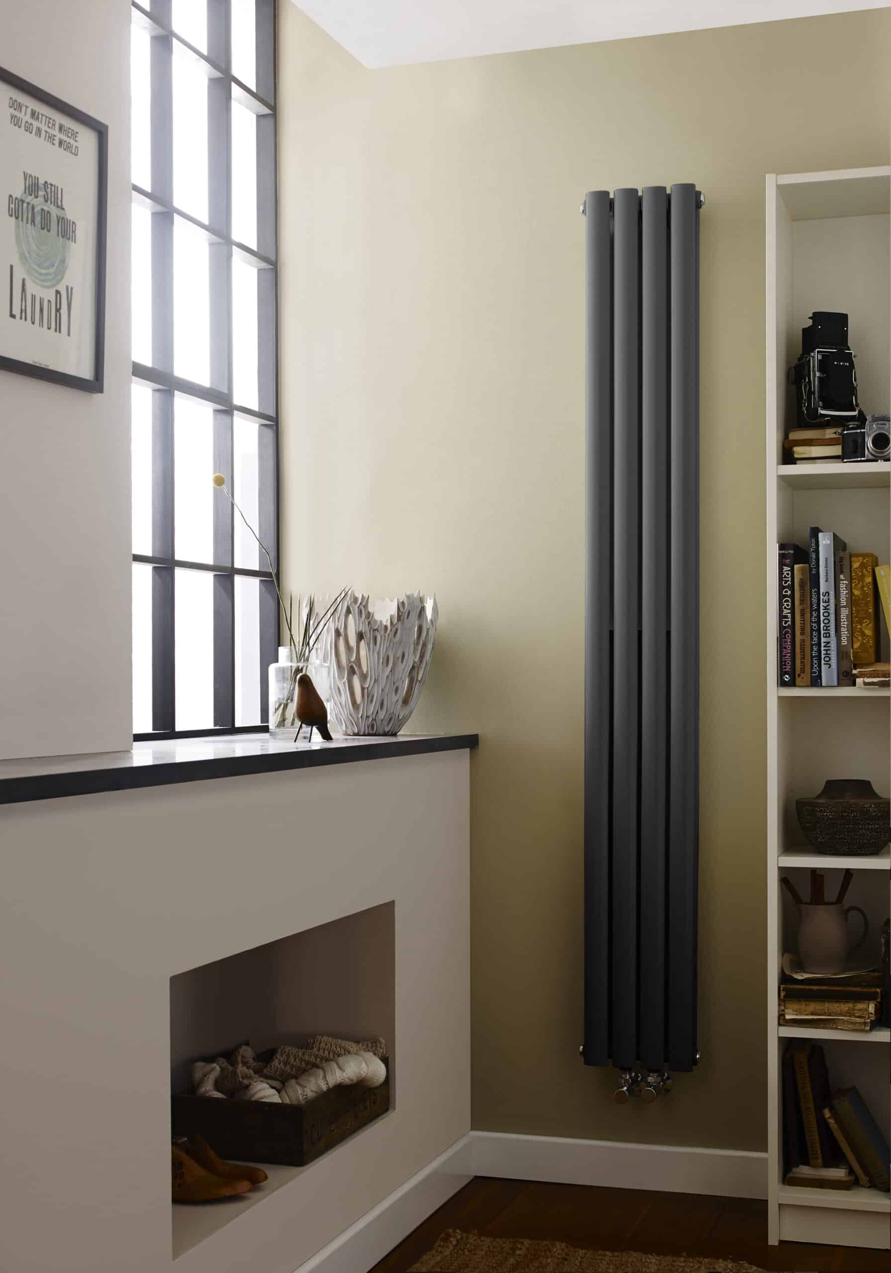 Sleek black vertical radiator in a modern bathroom with a window ledge decorated with ornaments and a white bookshelf, showcasing contemporary bathroom design and effective space heating solutions.