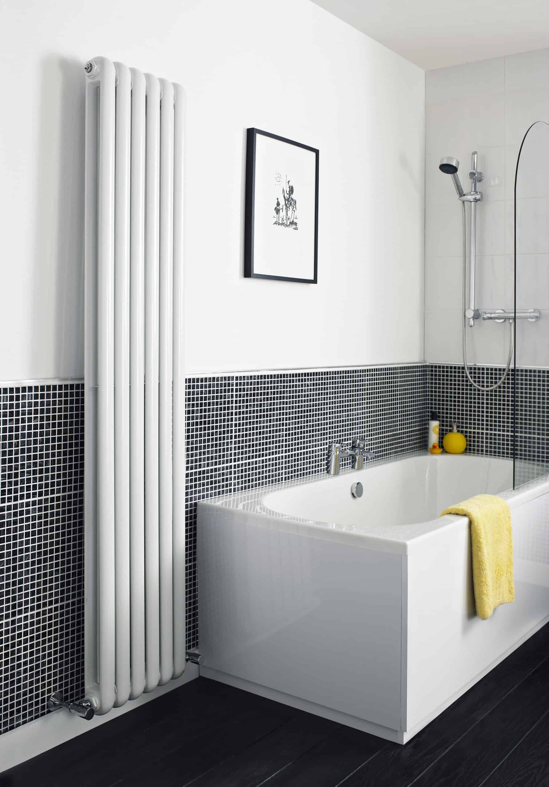 Contemporary white bathtub with sleek design in modern bathroom with black and white mosaic tiles, yellow towel, showerhead, and minimalist decor, featuring a vertical white radiator.