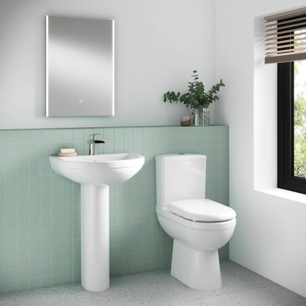 Modern white bathroom sink and toilet with green tiled wall, minimalist mirror and natural light for contemporary bathroom design.